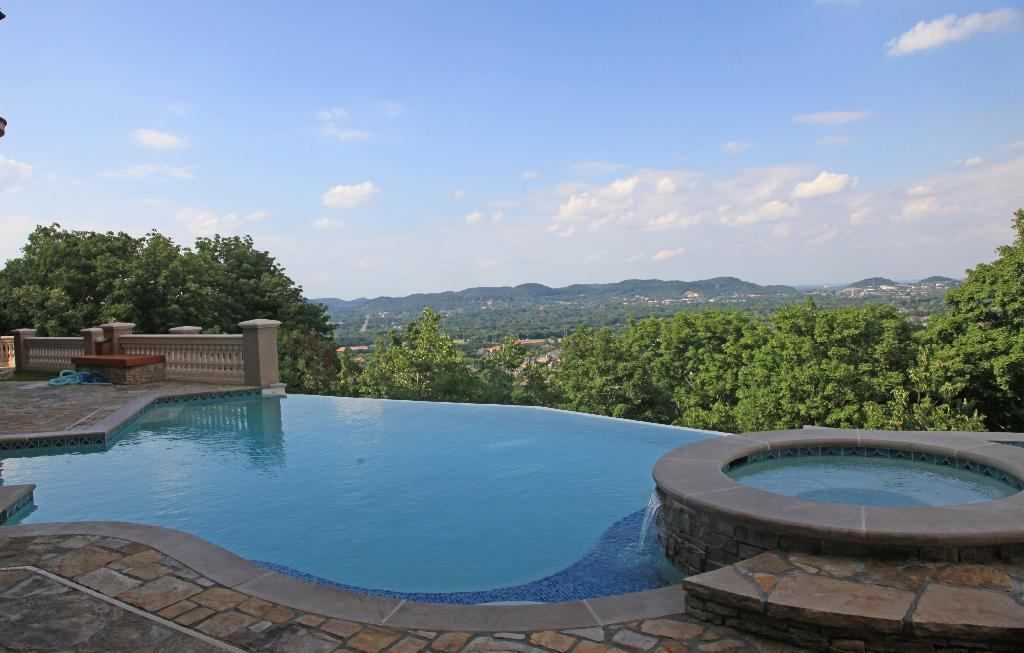 Infinity pool overlooking a valley with trees and a blue sky. A spa is on the right.