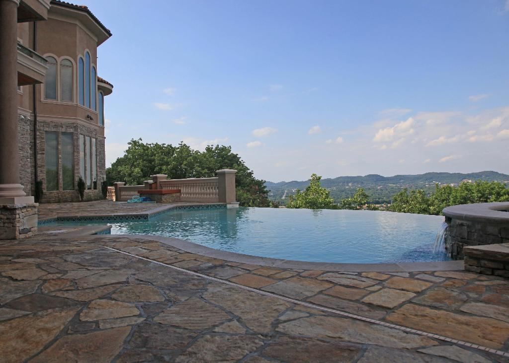 An infinity pool overlooks a scenic landscape from a luxurious house on a bright day.
