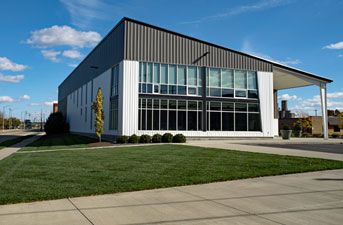 Modern building with white and dark gray siding, large windows, and a grassy lawn.