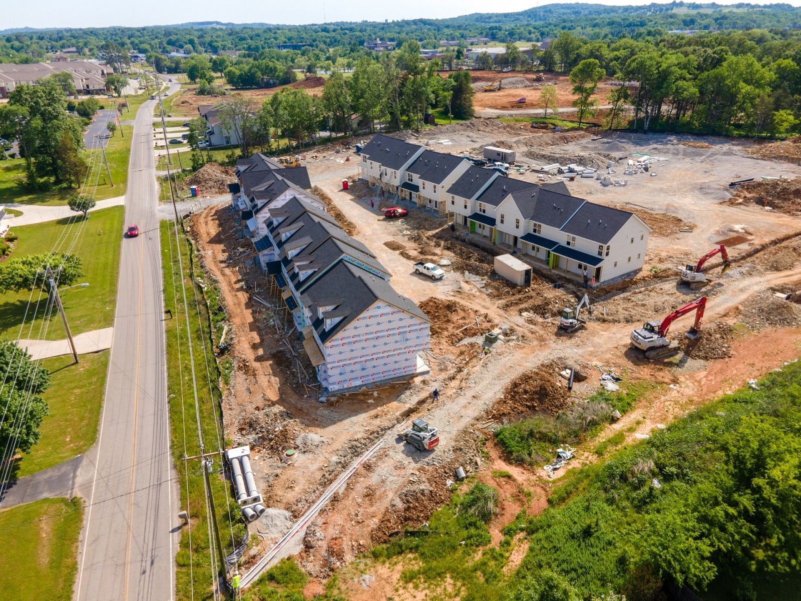 Aerial view of a construction site with townhomes under construction, excavators, and road.
