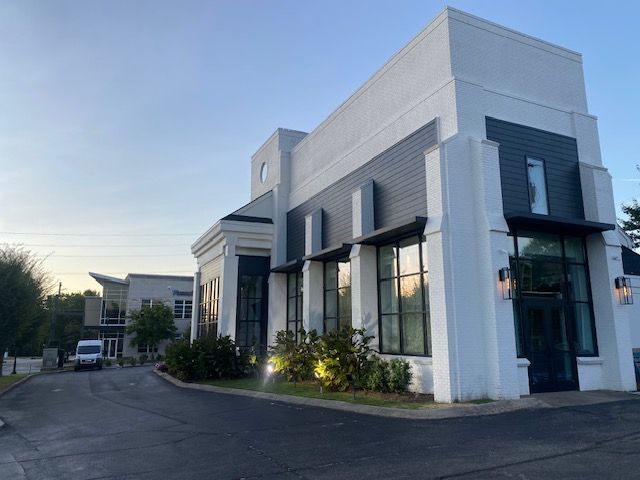 Modern building with white and dark gray accents, large windows, and an overcast sky.