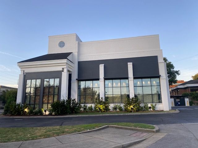 Modern white and charcoal building with large windows and landscaping, under a blue sky.