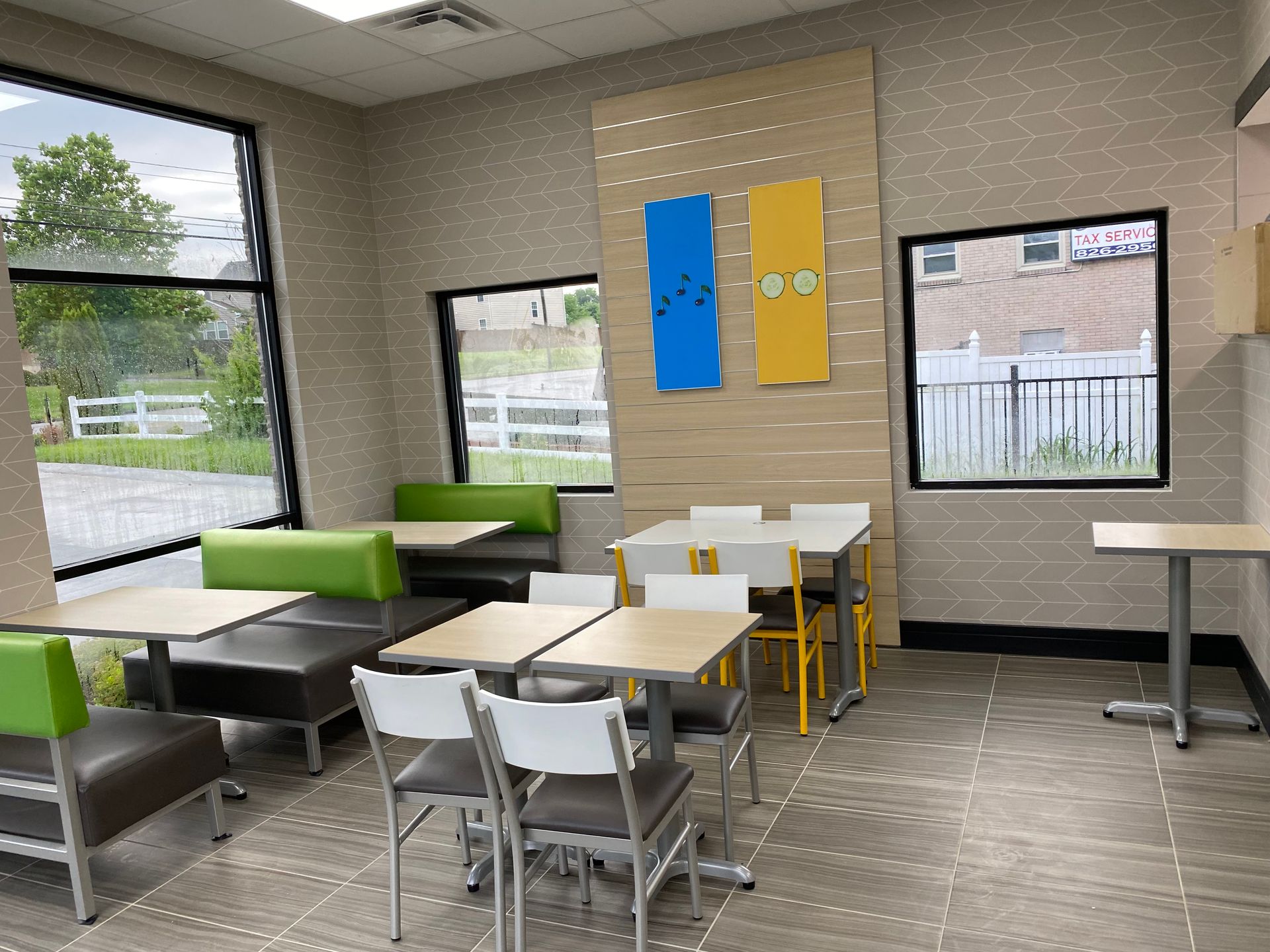 Restaurant interior with tables and chairs near windows, green and brown booth seating.