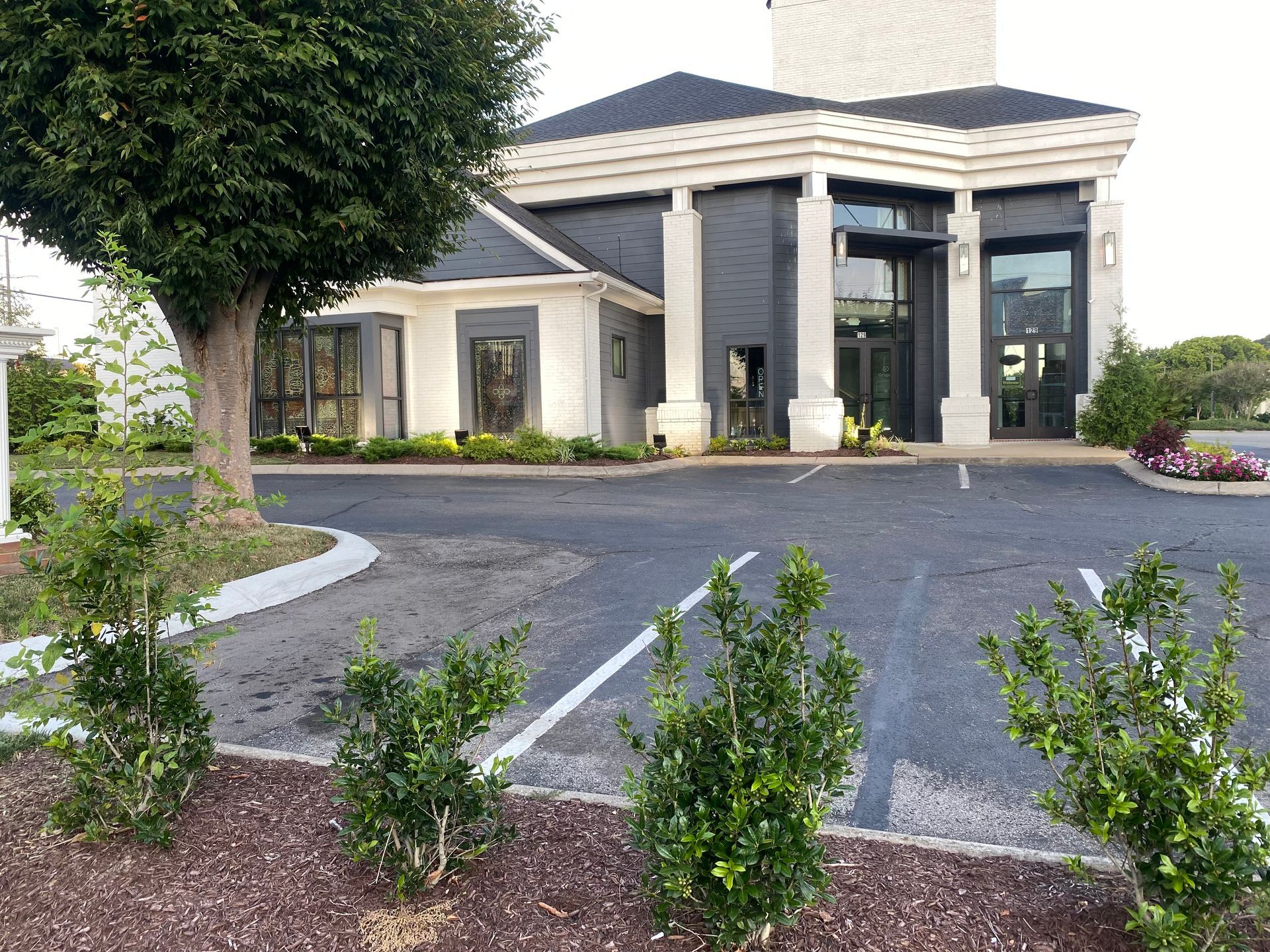 Modern building with dark accents, tall columns, and manicured landscaping, empty parking lot.