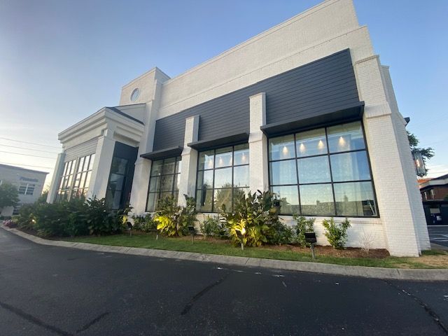Modern white brick building with black awning and large windows. Landscaping in front.
