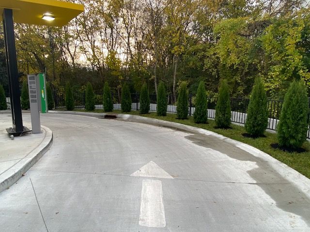 Driveway with directional arrow at a gas station, lined with green trees against a backdrop of fall foliage.