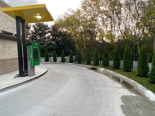 Drive-thru lane with order kiosk and canopy; evergreen trees line the curb.