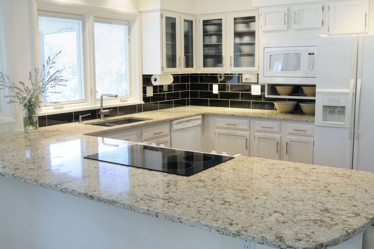 Bright modern kitchen with white cabinets, black countertops, and a large speckled island countertop