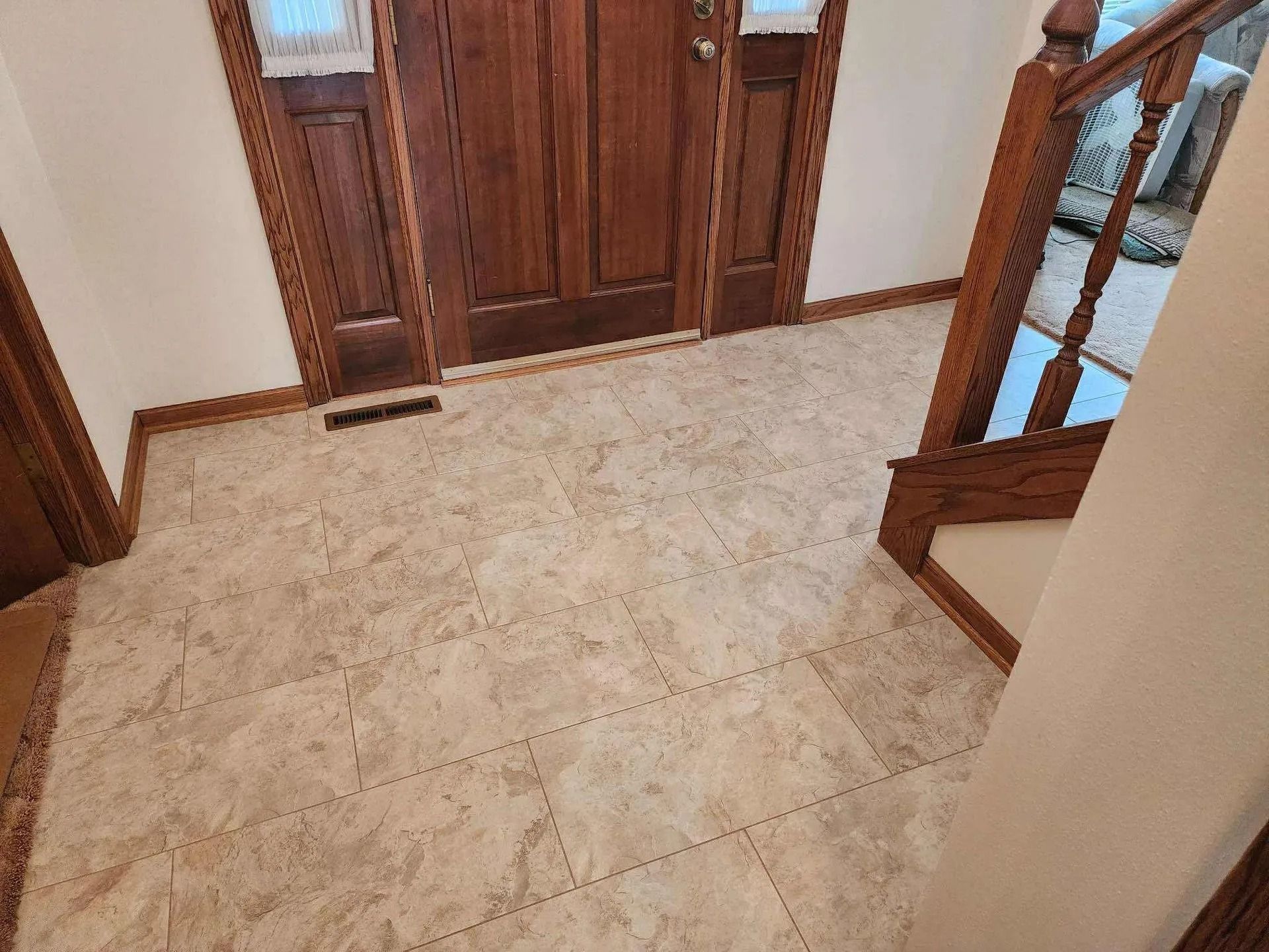 Tiled hallway with wooden double doors and a staircase railing on the right.