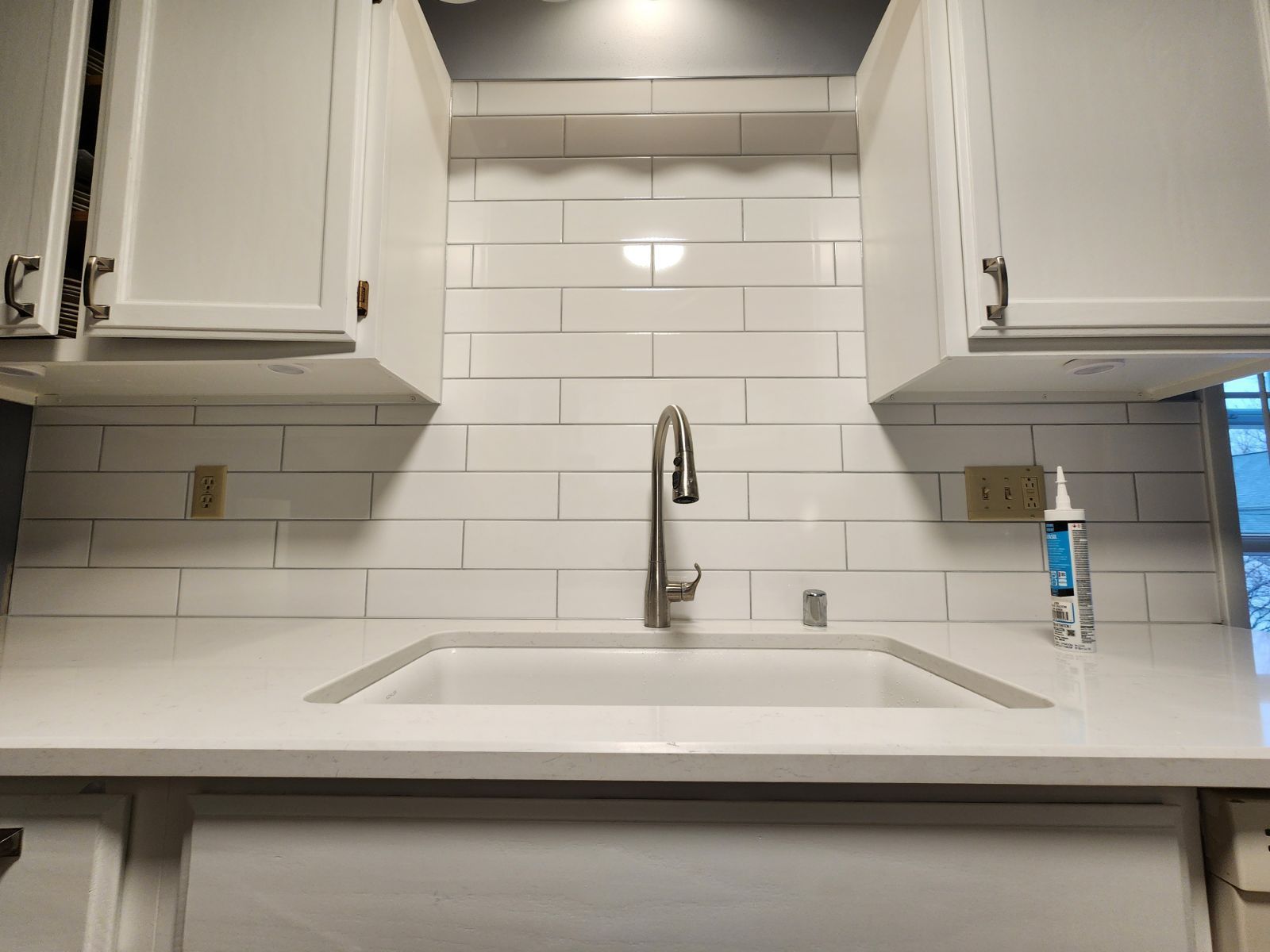 White kitchen sink with subway tile backsplash, chrome faucet, and white cabinets