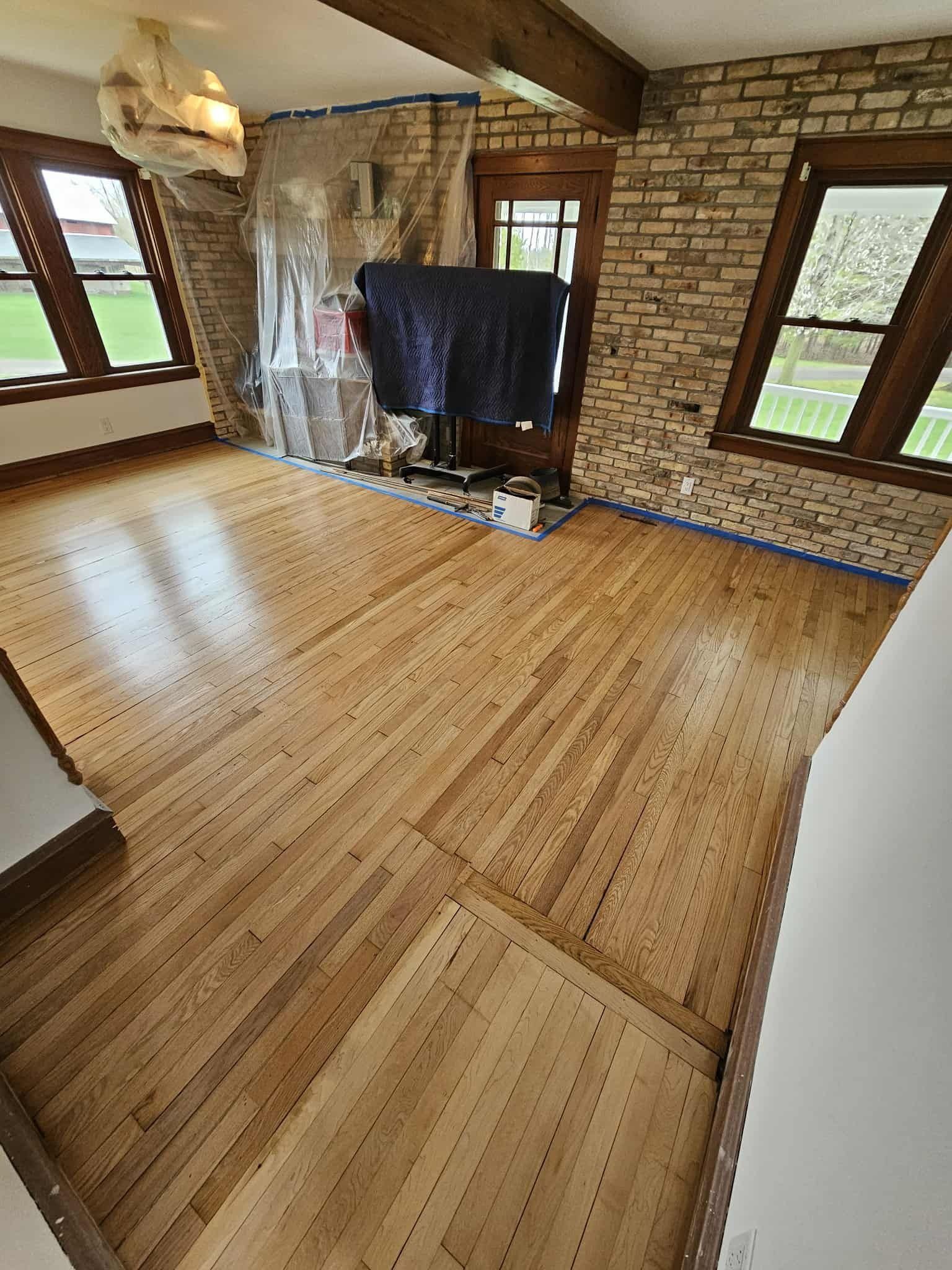 Empty room with unfinished wood floors, brick walls, and windows covered in plastic sheeting