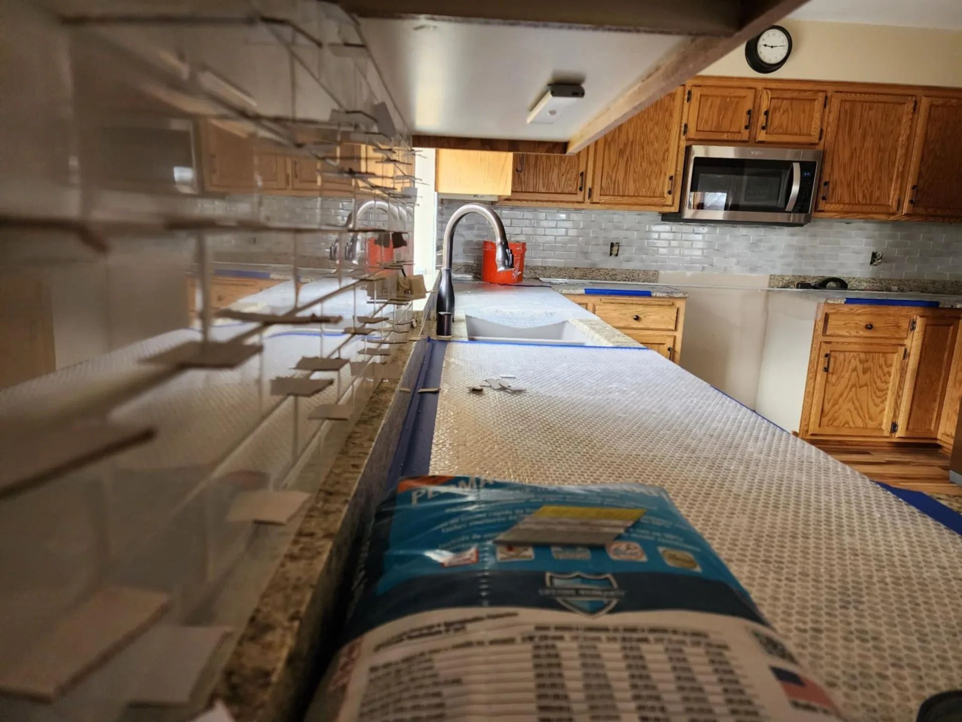 Kitchen interior with long countertop, wooden cabinets, stainless appliances, and a red kettle near the sink.