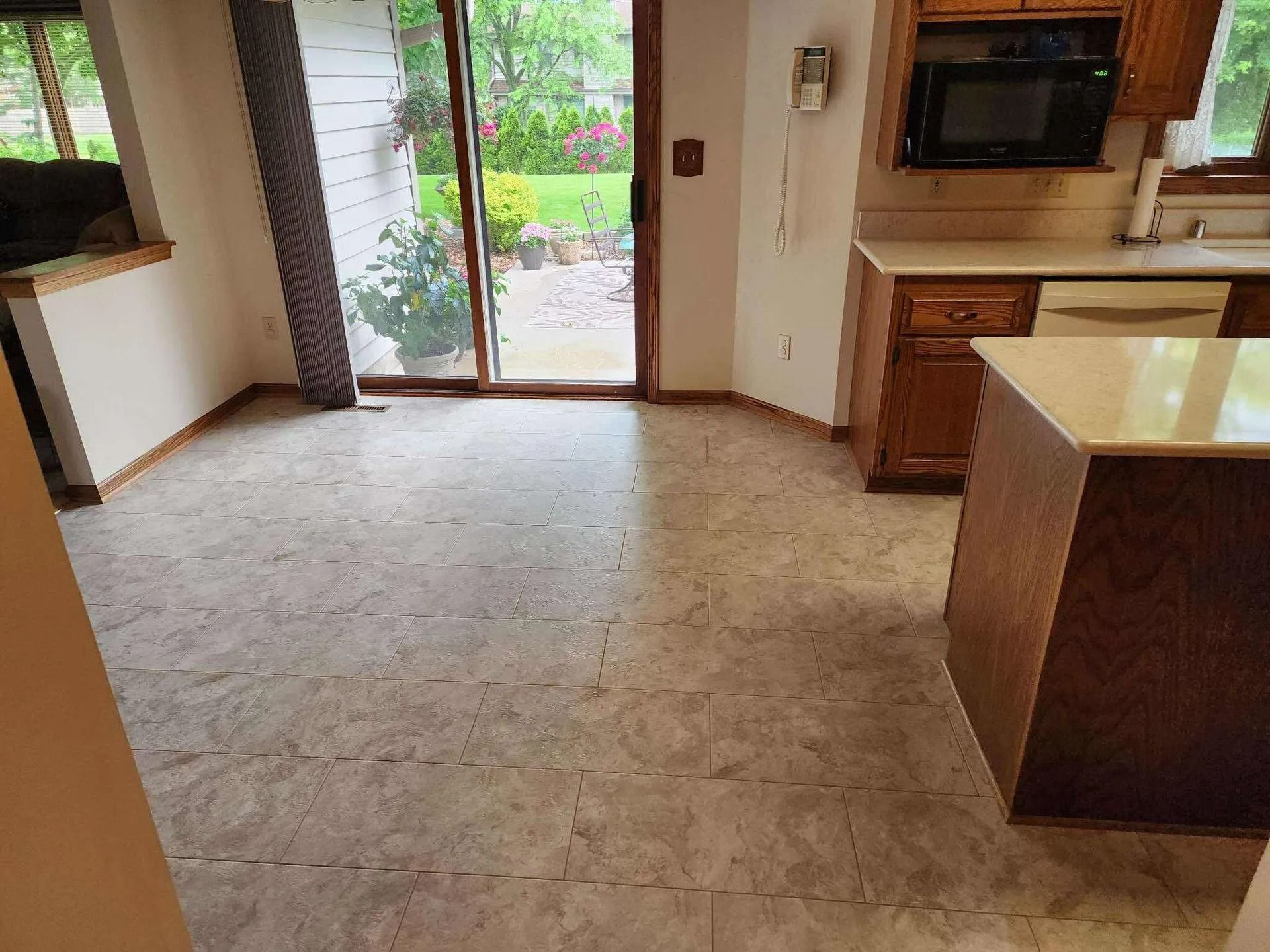Empty kitchen with tiled floor, island counter, and sliding glass door to a garden.