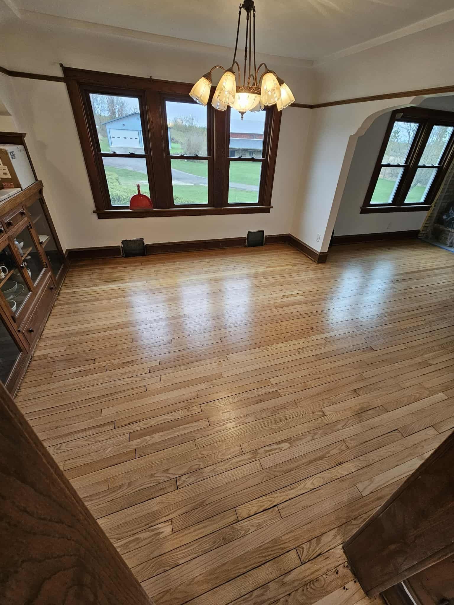 Empty dining room with large windows, hardwood floors, and a hanging light fixture.