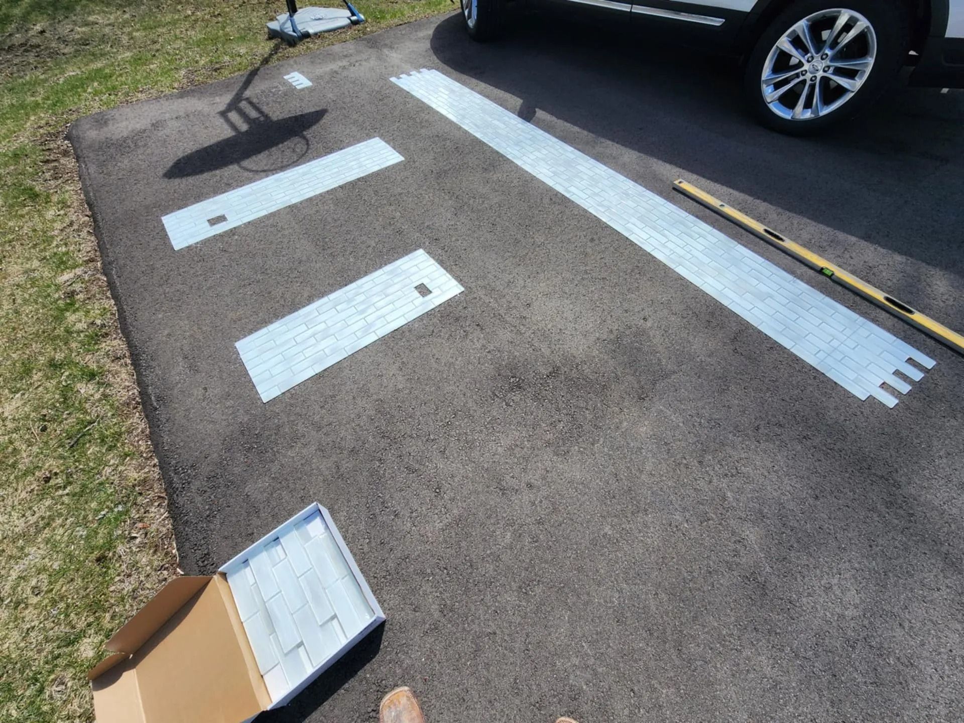 Two white parking stencils and a black car on asphalt next to grass, with a cardboard box in the foreground