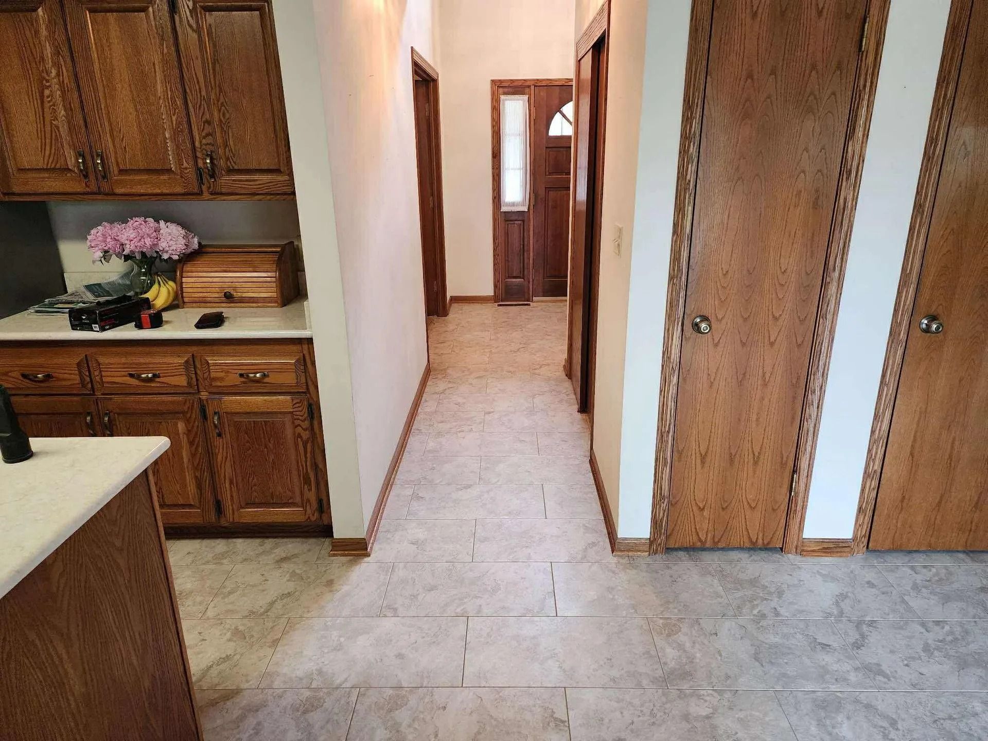 Narrow hallway with tile floor, wooden cabinets on the left, and wood-paneled doors on the right.