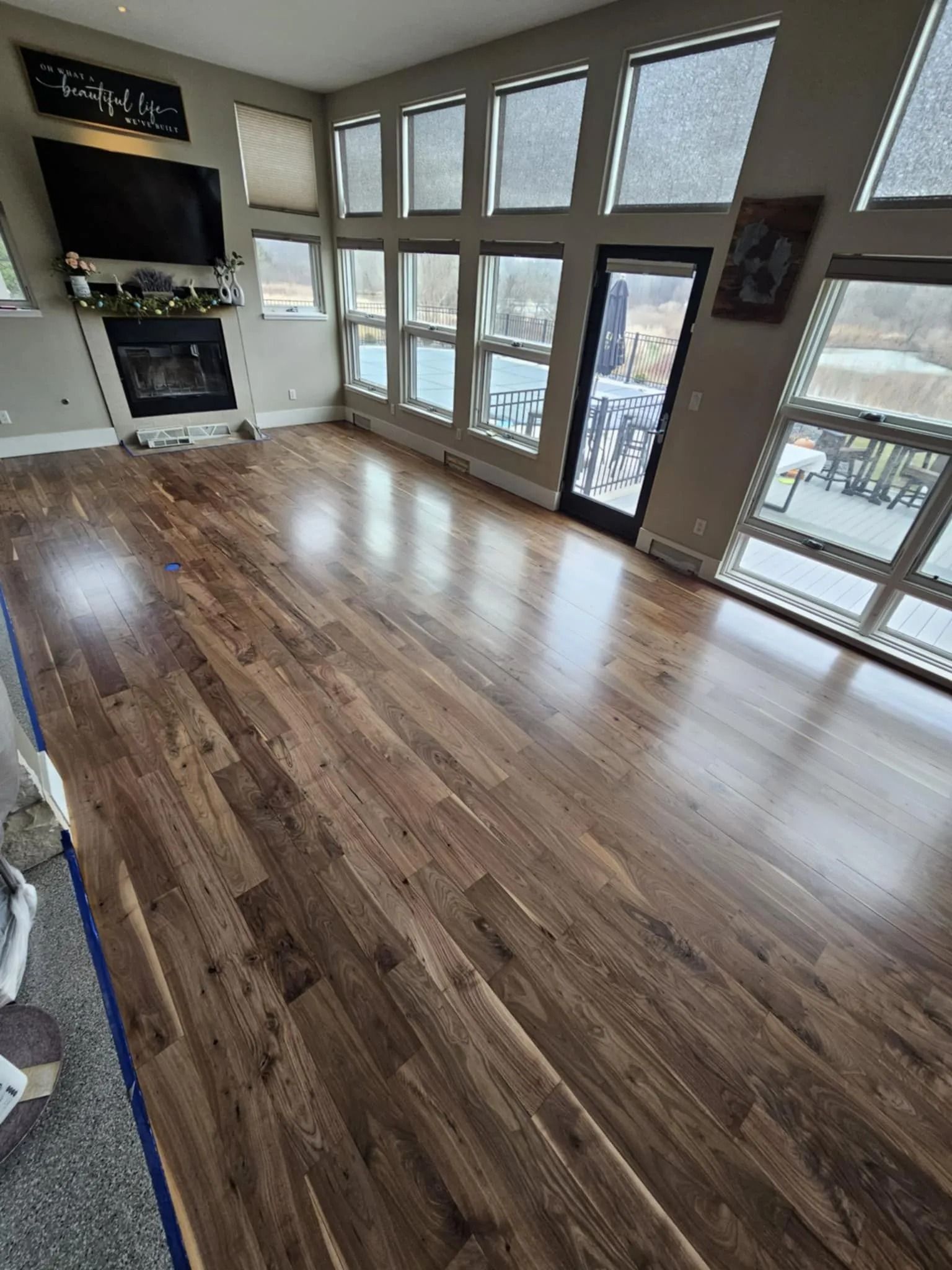 Empty modern room with wood floors, large windows, and a kitchen area on the left.