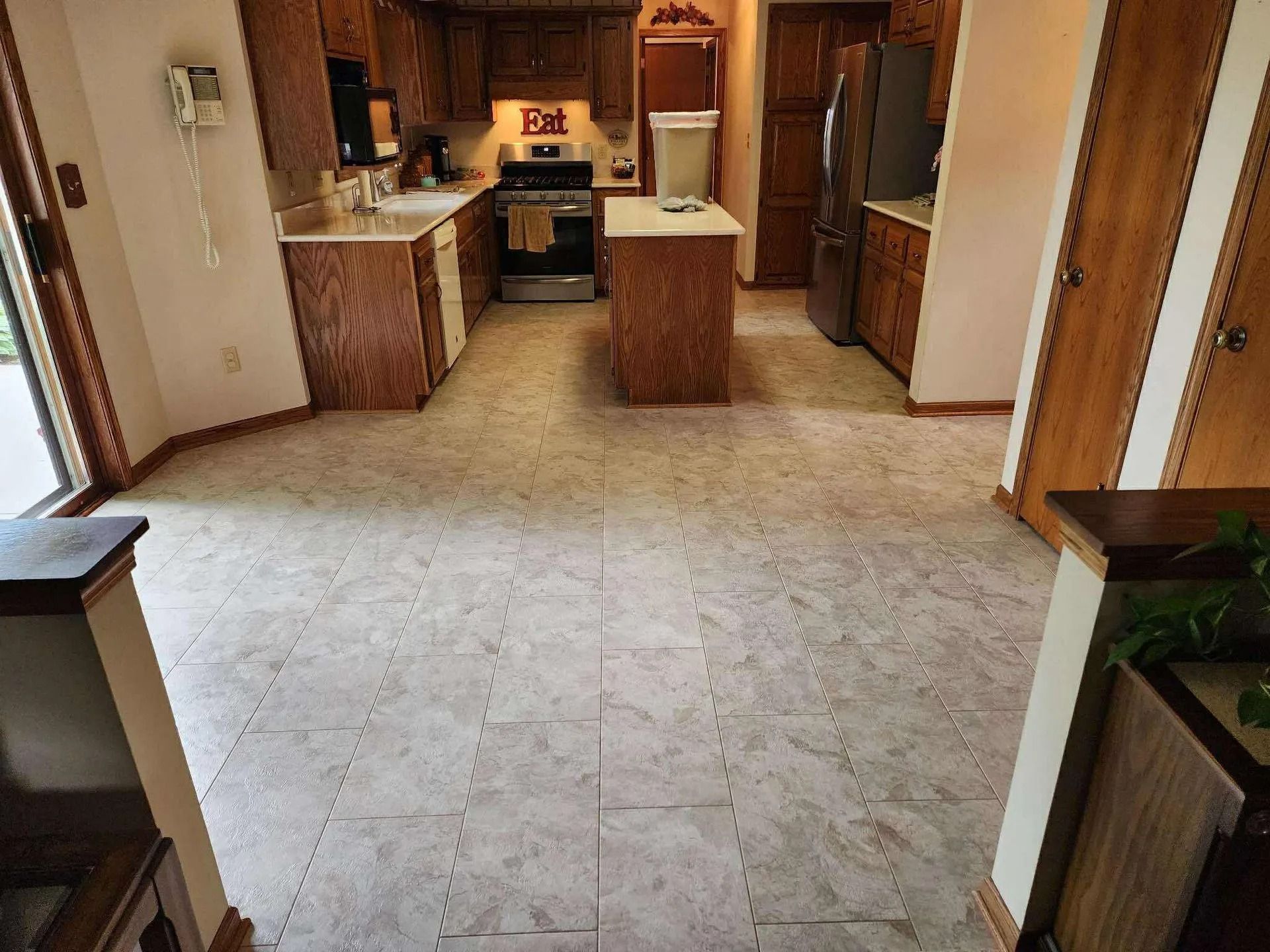 Empty kitchen with beige tile floor, wooden cabinets, and a stove in the back.