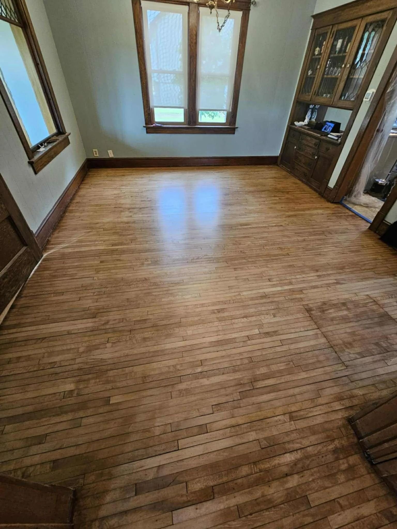 Empty room with light wood floor, windows, and built-in cabinets.