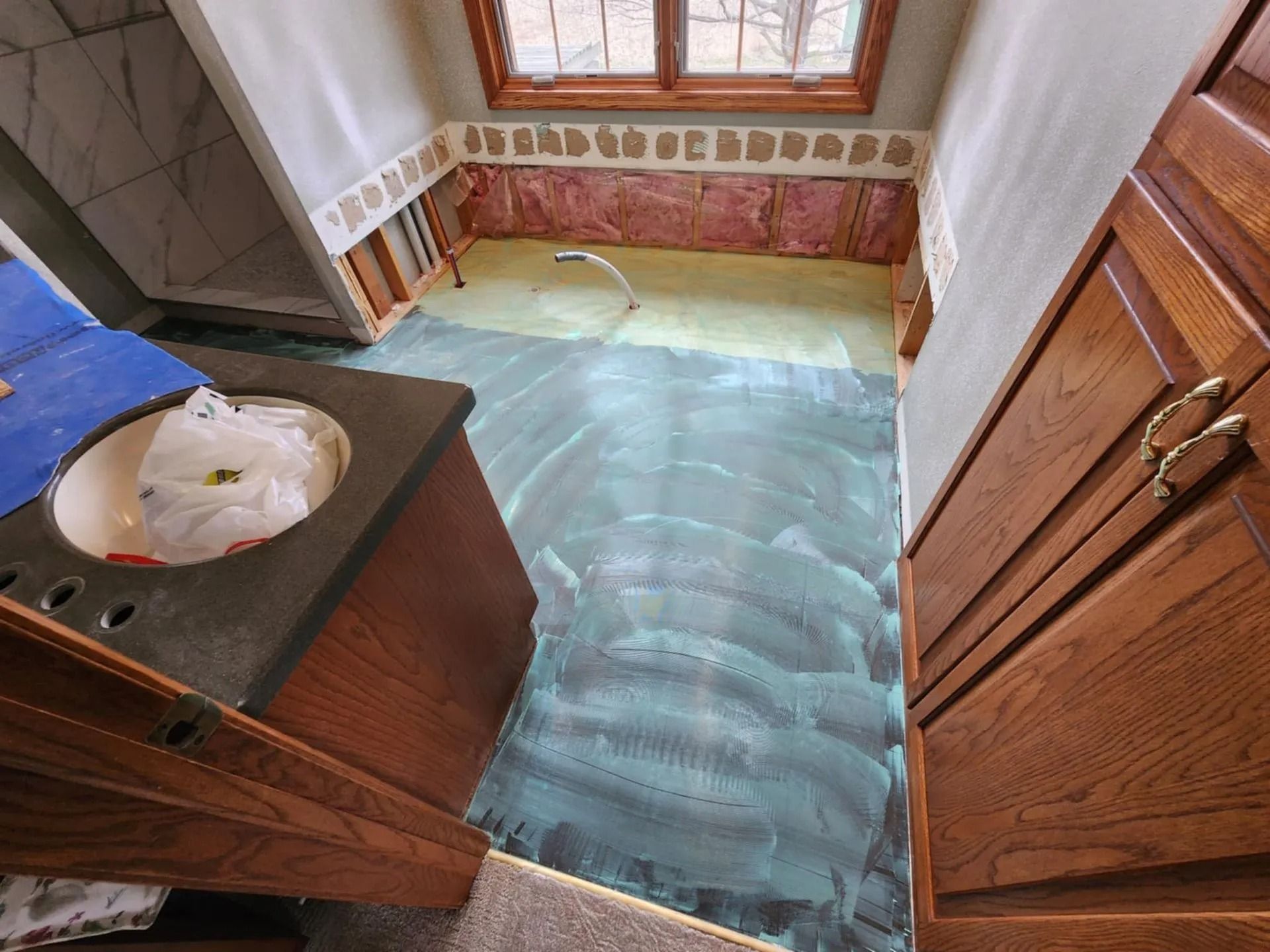 Flooded bathroom with standing water, wooden cabinets, and a window over the sink.