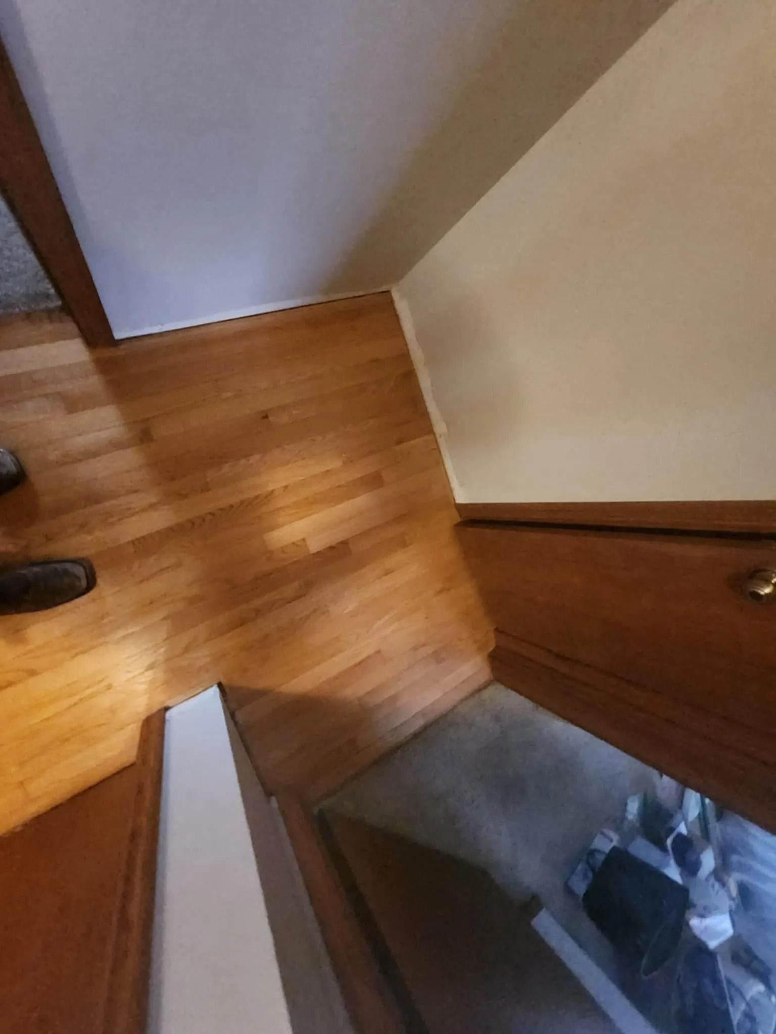 Top of a wooden staircase with beige walls and a glimpse of shoes below.