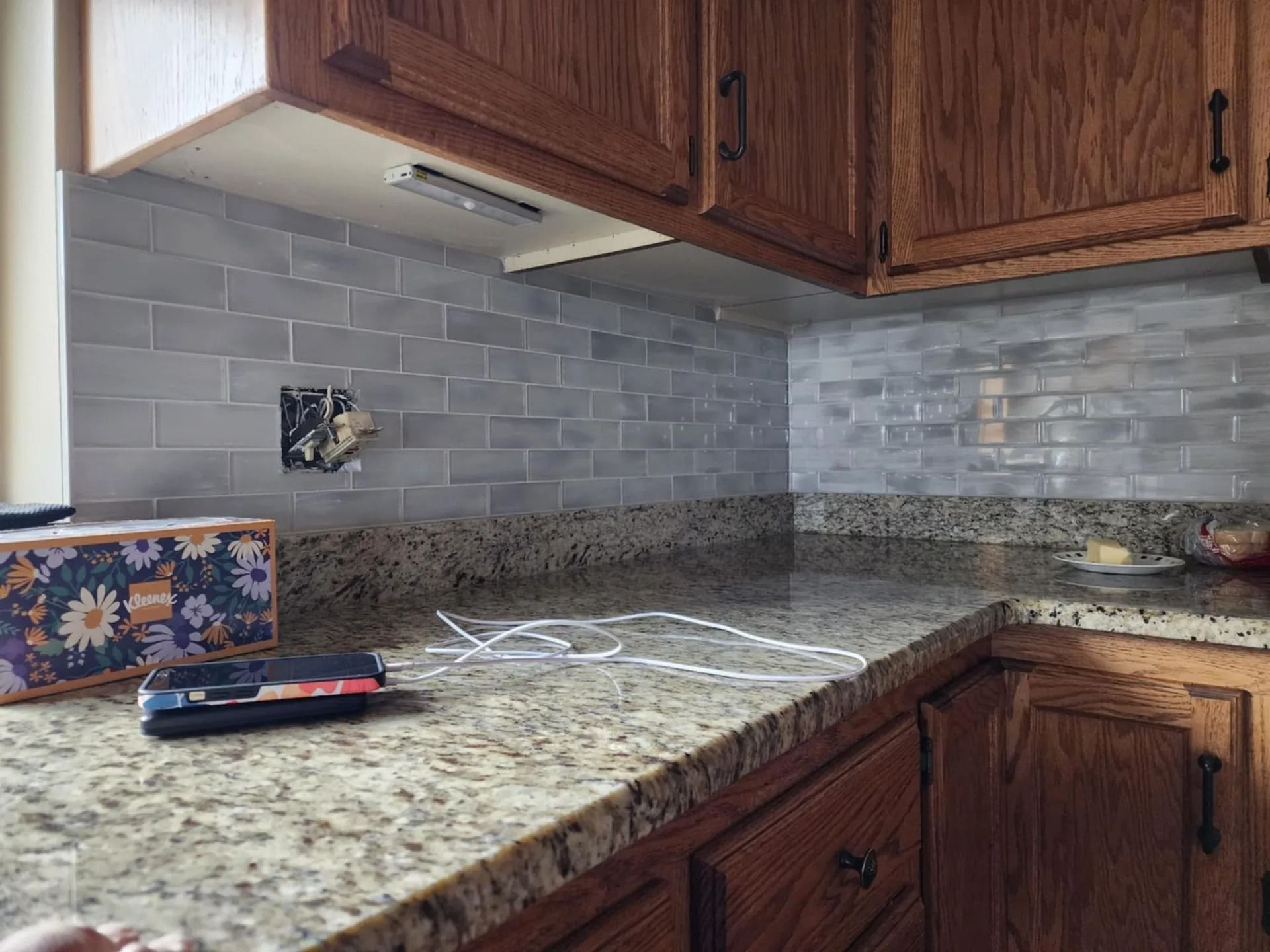 Corner kitchen countertop with granite surfaces, gray tile backsplash, and dark wood cabinets
