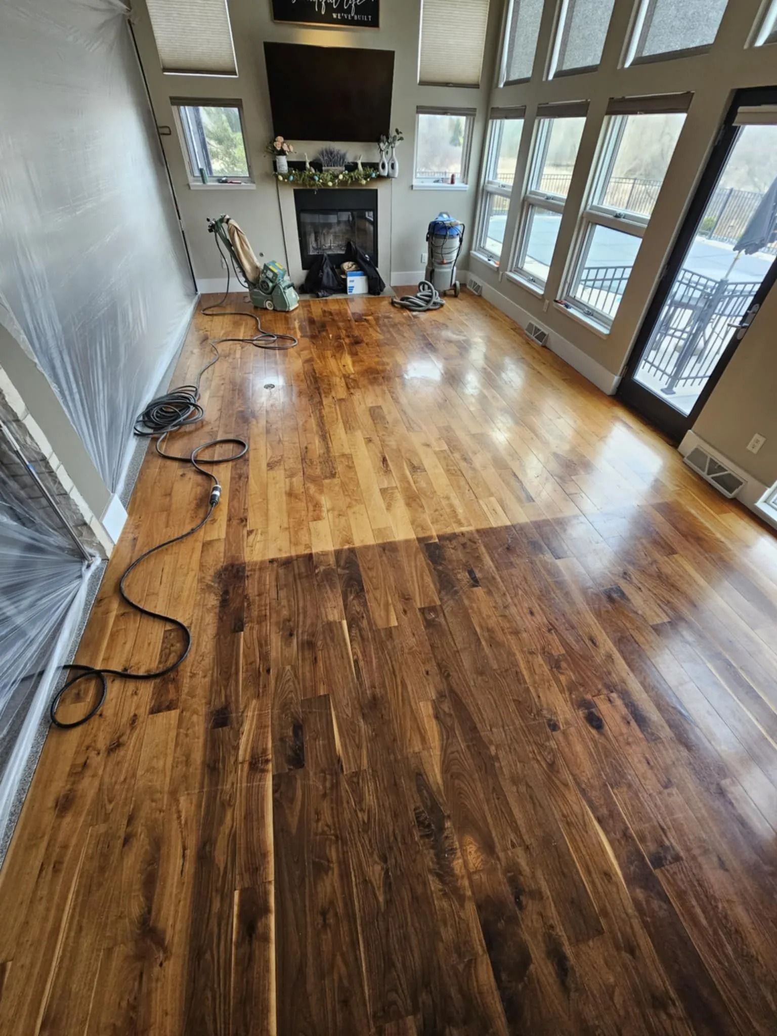 Empty sunroom with hardwood floors, large windows, fireplace, and a few cords along the left wall.