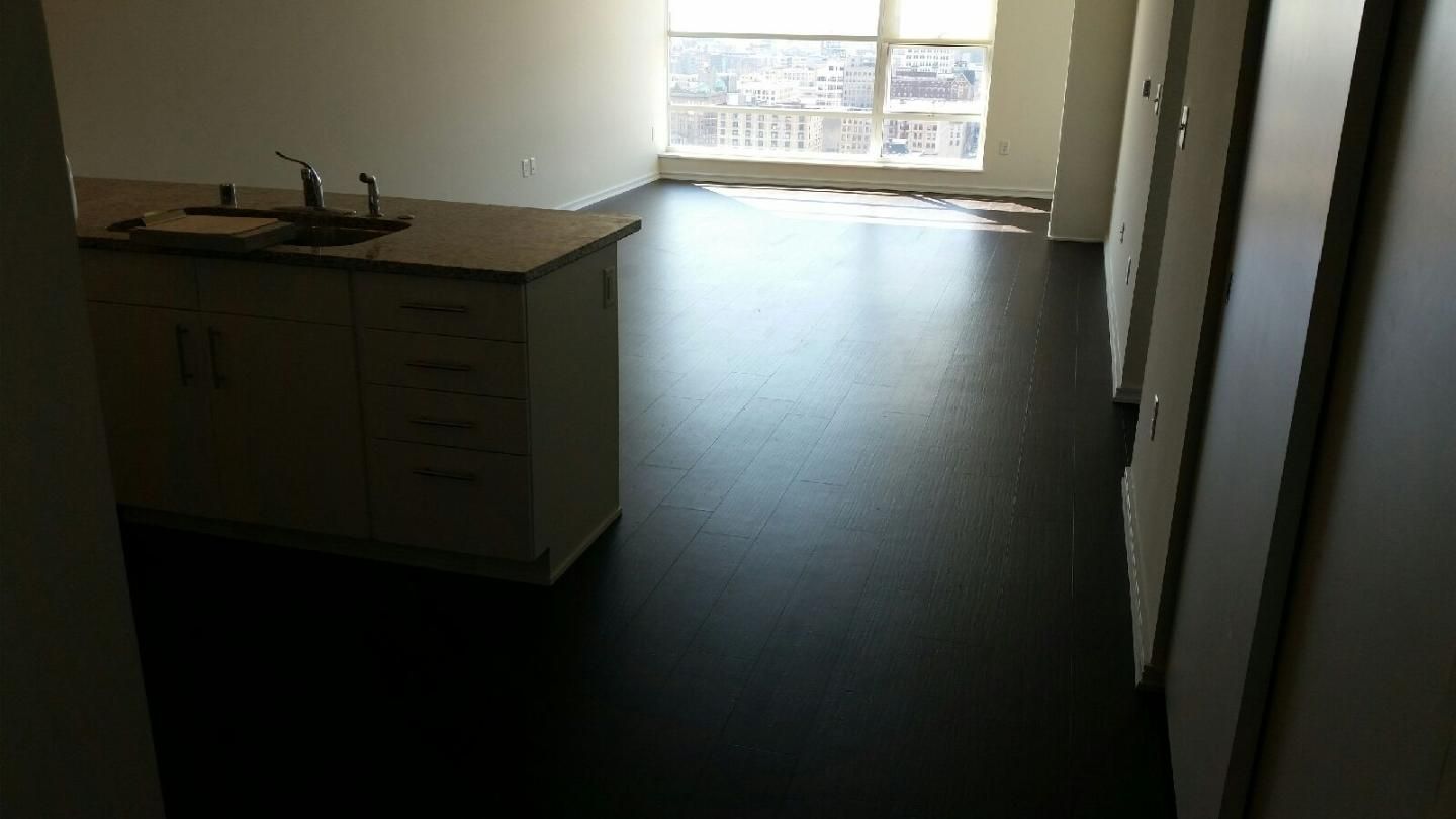 Empty apartment interior with a kitchen island and sunlight through a large window.
