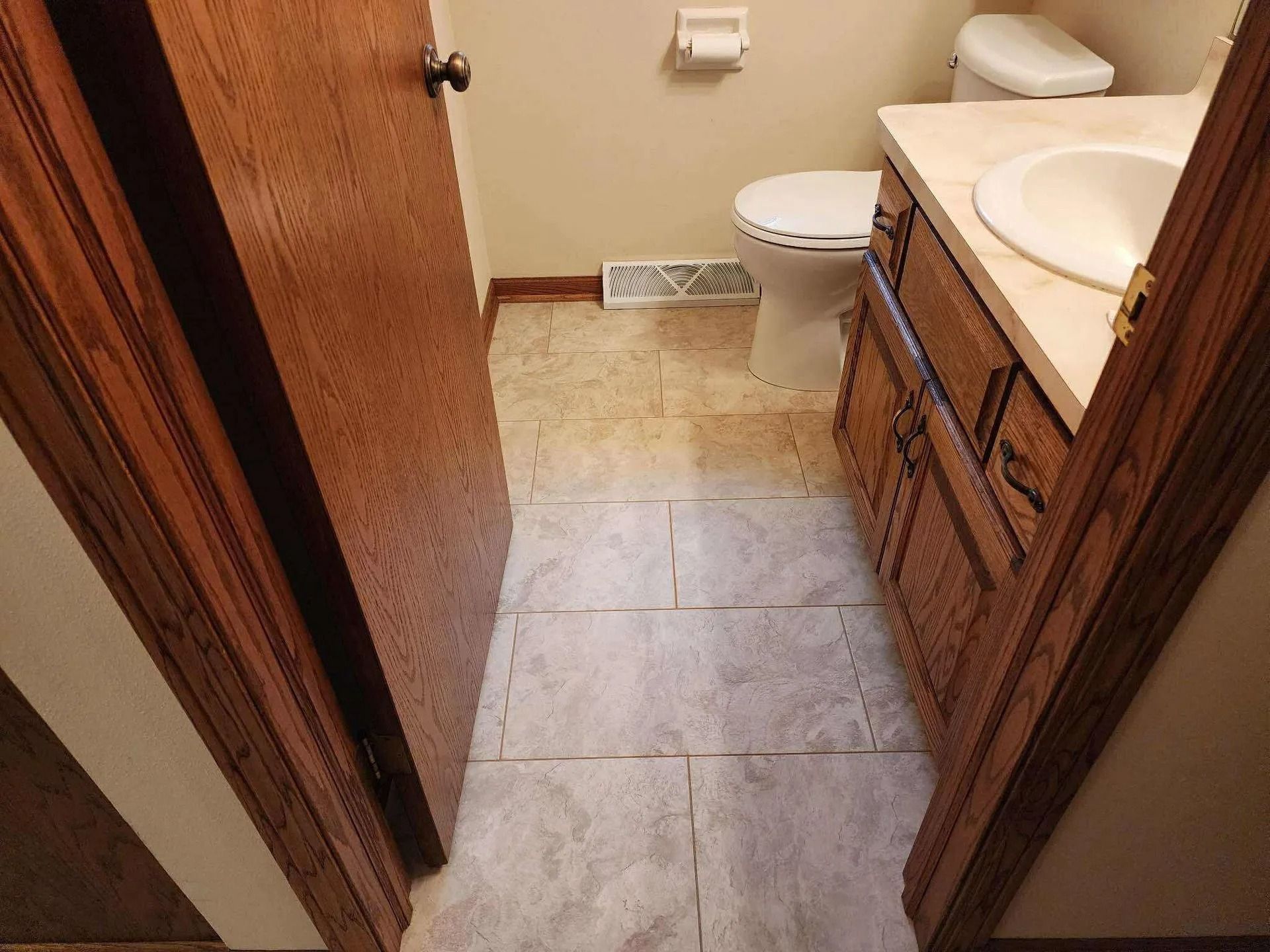 Small bathroom with tile floor, vanity sink, toilet, and wood cabinets viewed from the doorway