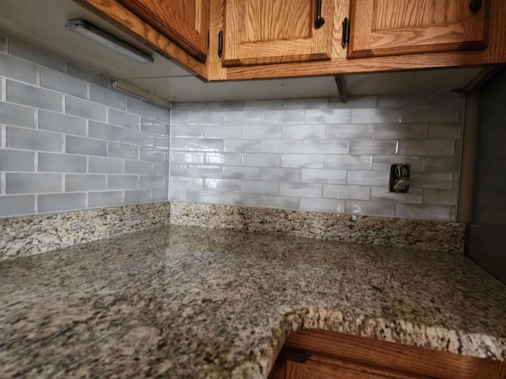Kitchen corner with granite countertop, white subway tile backsplash, and wooden cabinets
