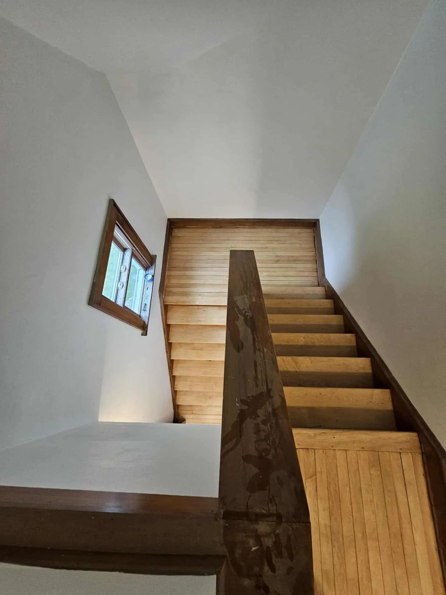 Indoor stairwell with wooden steps, white walls, and a small window on the left.