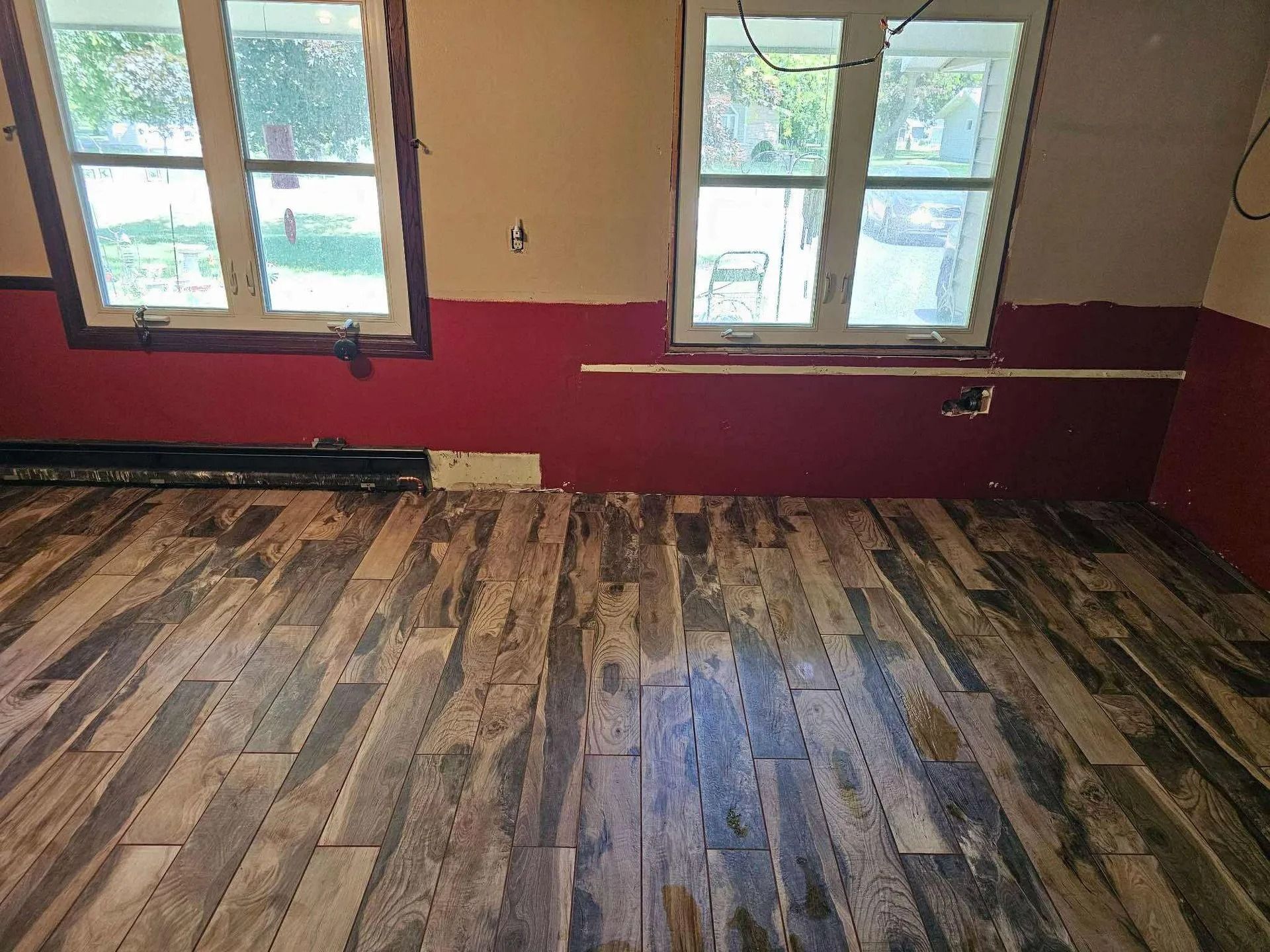 Empty room with hardwood floor, red walls, and two windows letting in daylight