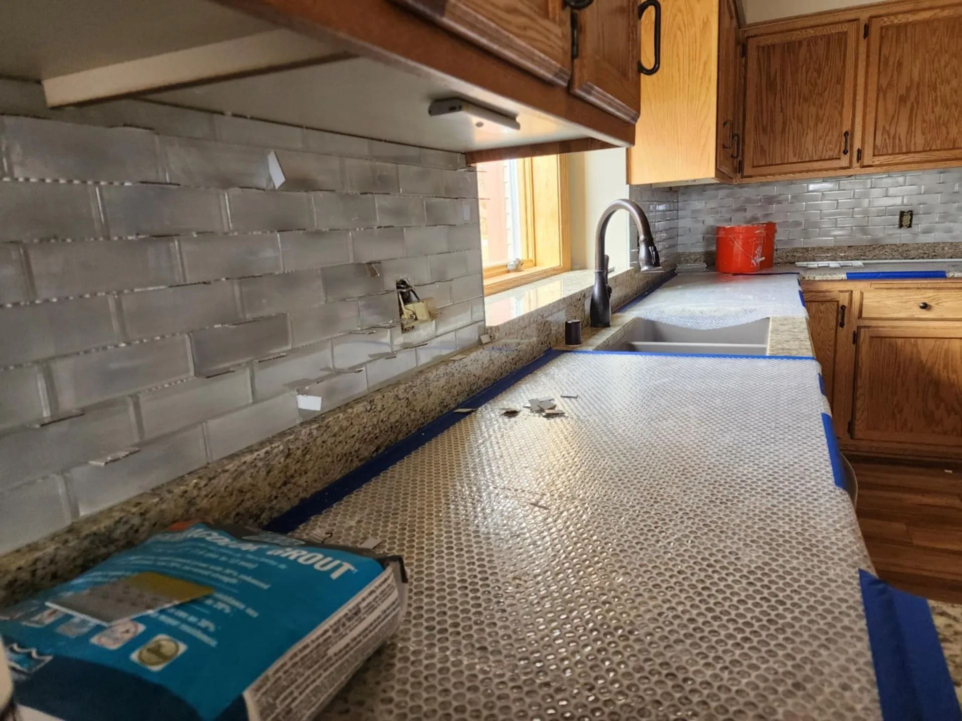 Kitchen countertop covered with protective sheeting, tile backsplash, and a sink by a sunlit window