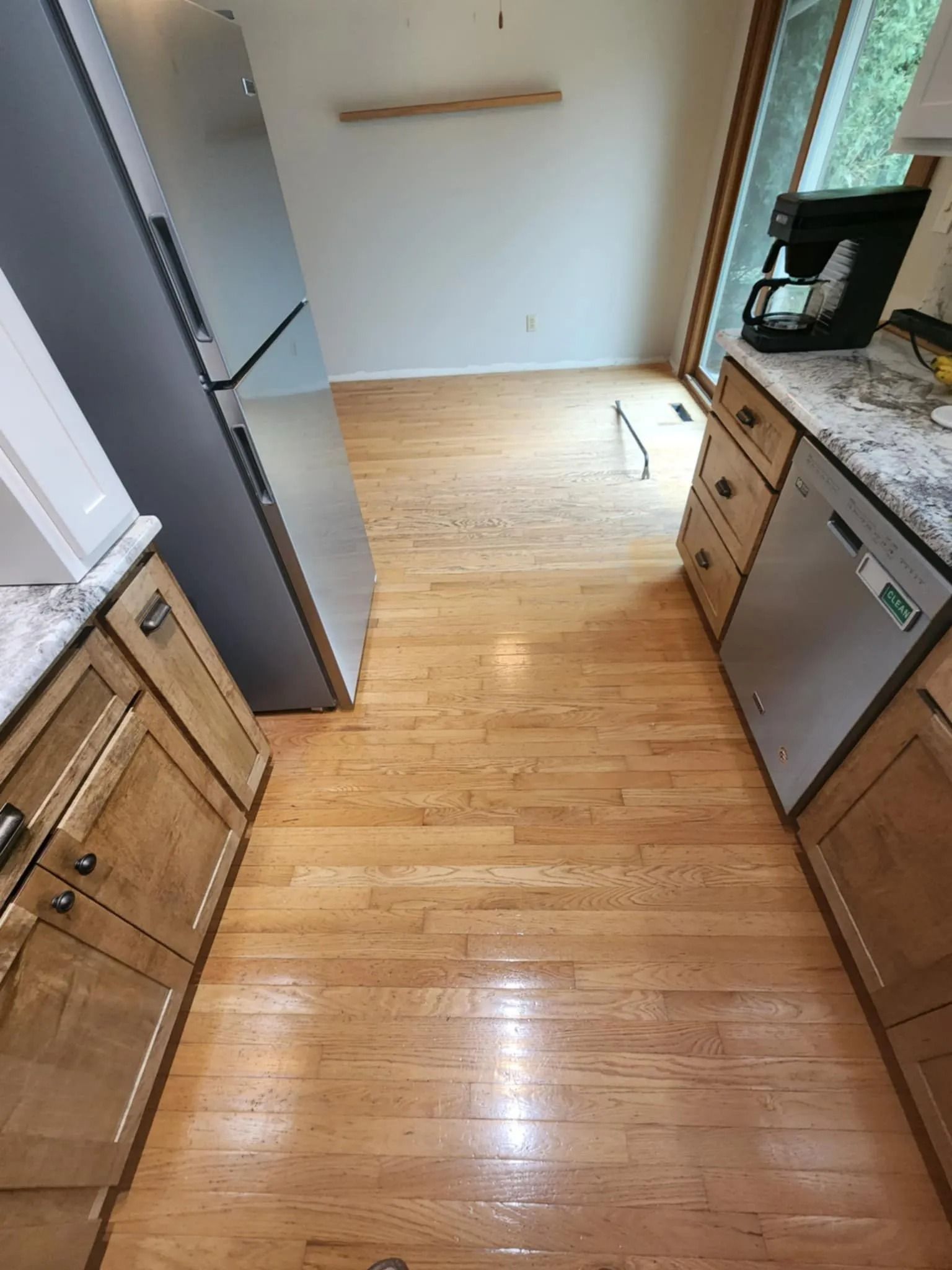 Narrow kitchen with wood floors, wooden cabinets, stainless fridge, and a dishwasher by the sink