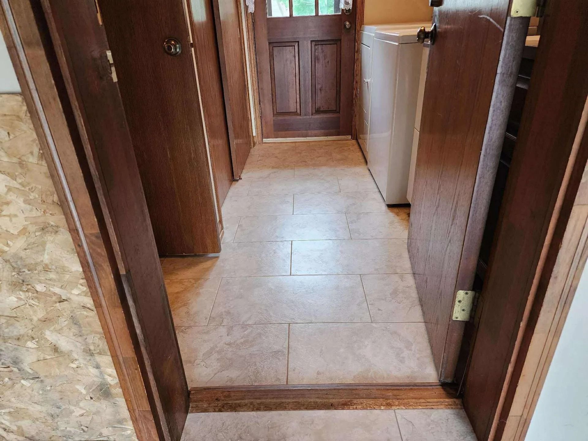 Narrow hallway with beige tile floor, wood-paneled walls, and a back door at the end