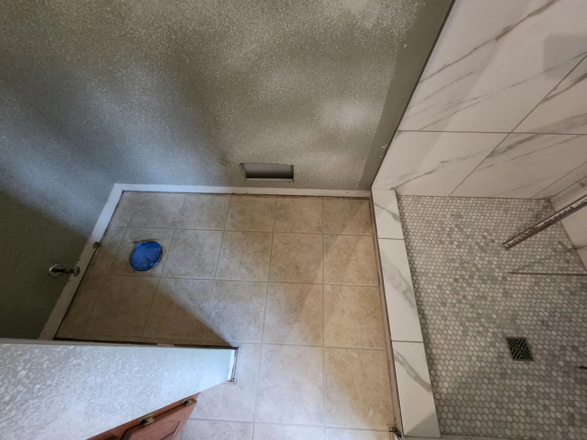 Bathroom corner with tan tile floor, blue bowl, and tiled shower area with drain