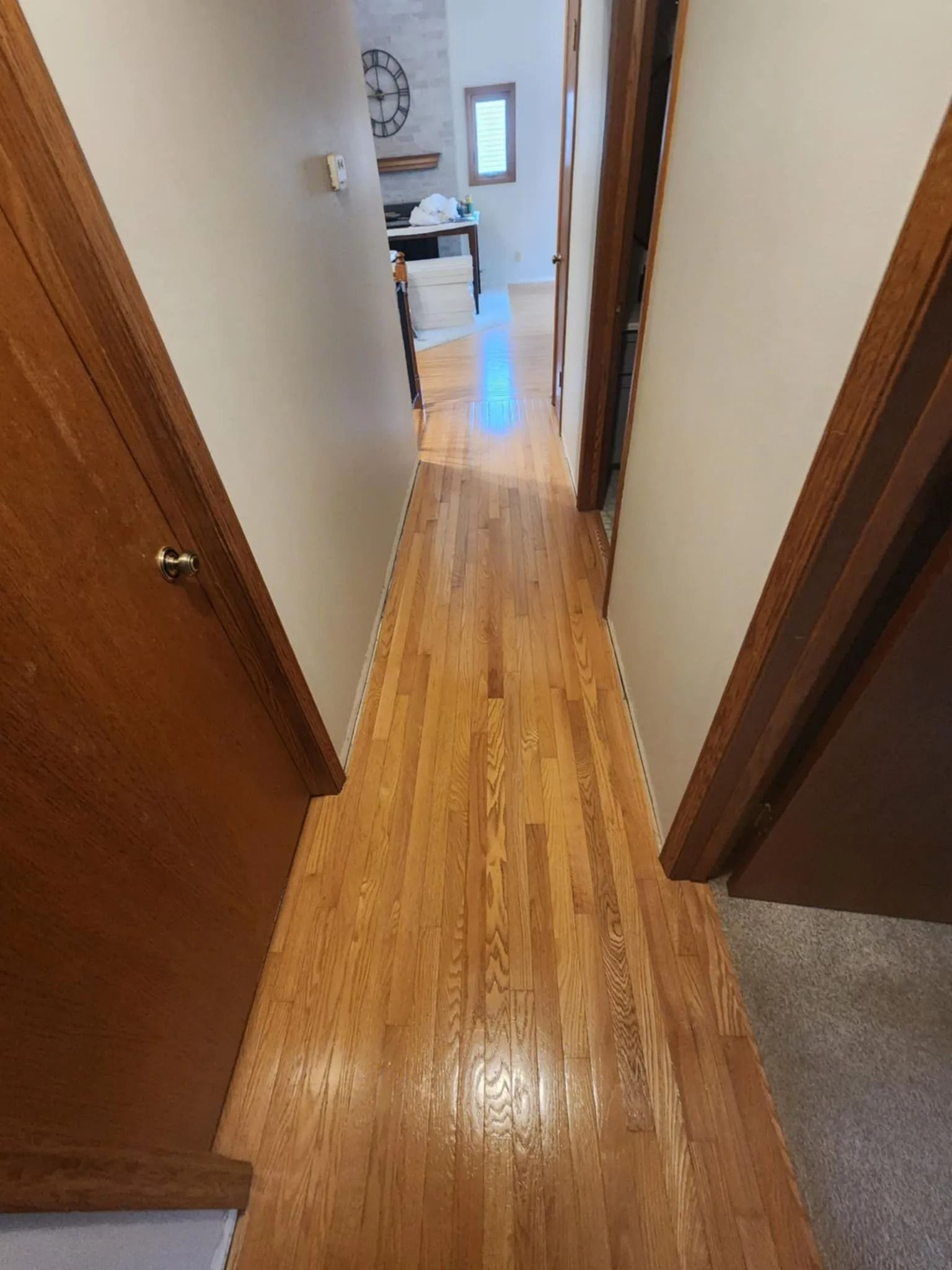 Narrow hallway with wood floors and doors, leading to a bright room at the end.