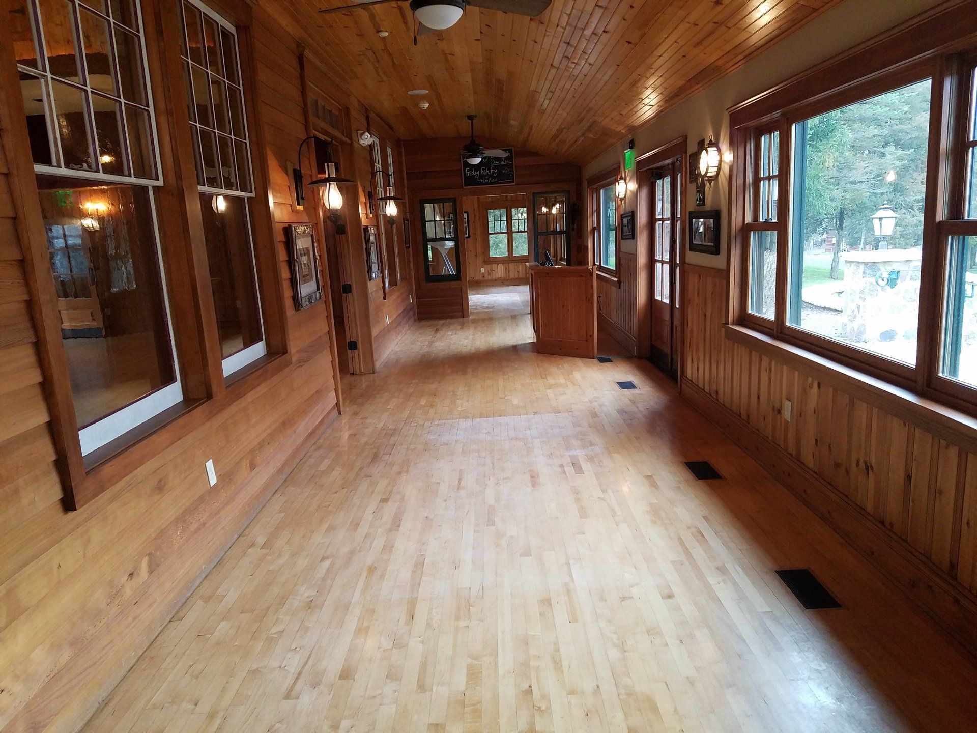 Wood-paneled empty hall with large windows, hardwood floor, and wall-mounted lights
