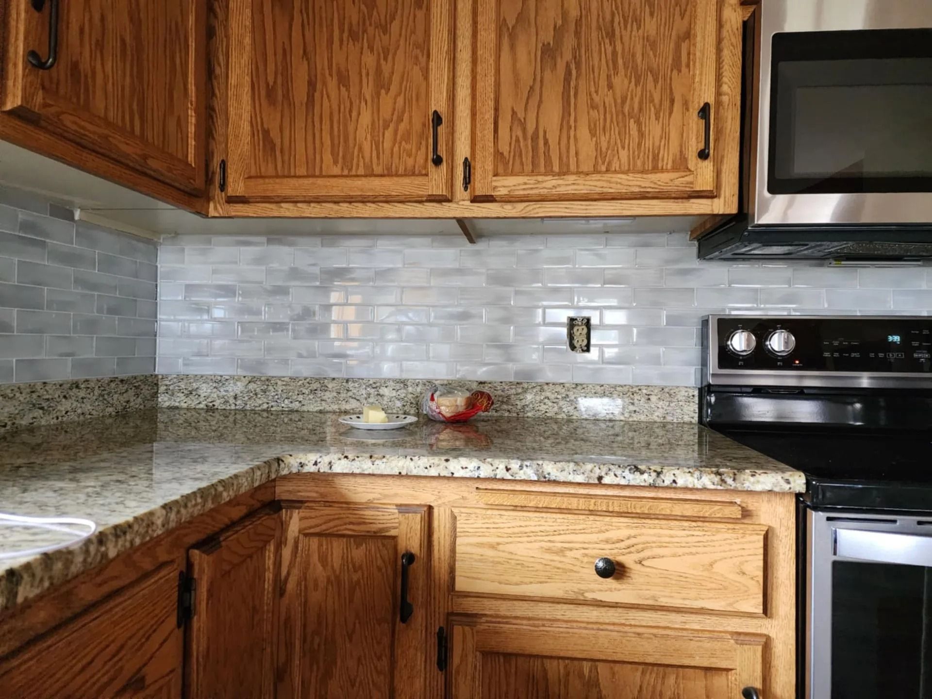 Kitchen corner with wood cabinets, granite countertops, tiled backsplash, and stainless steel stove