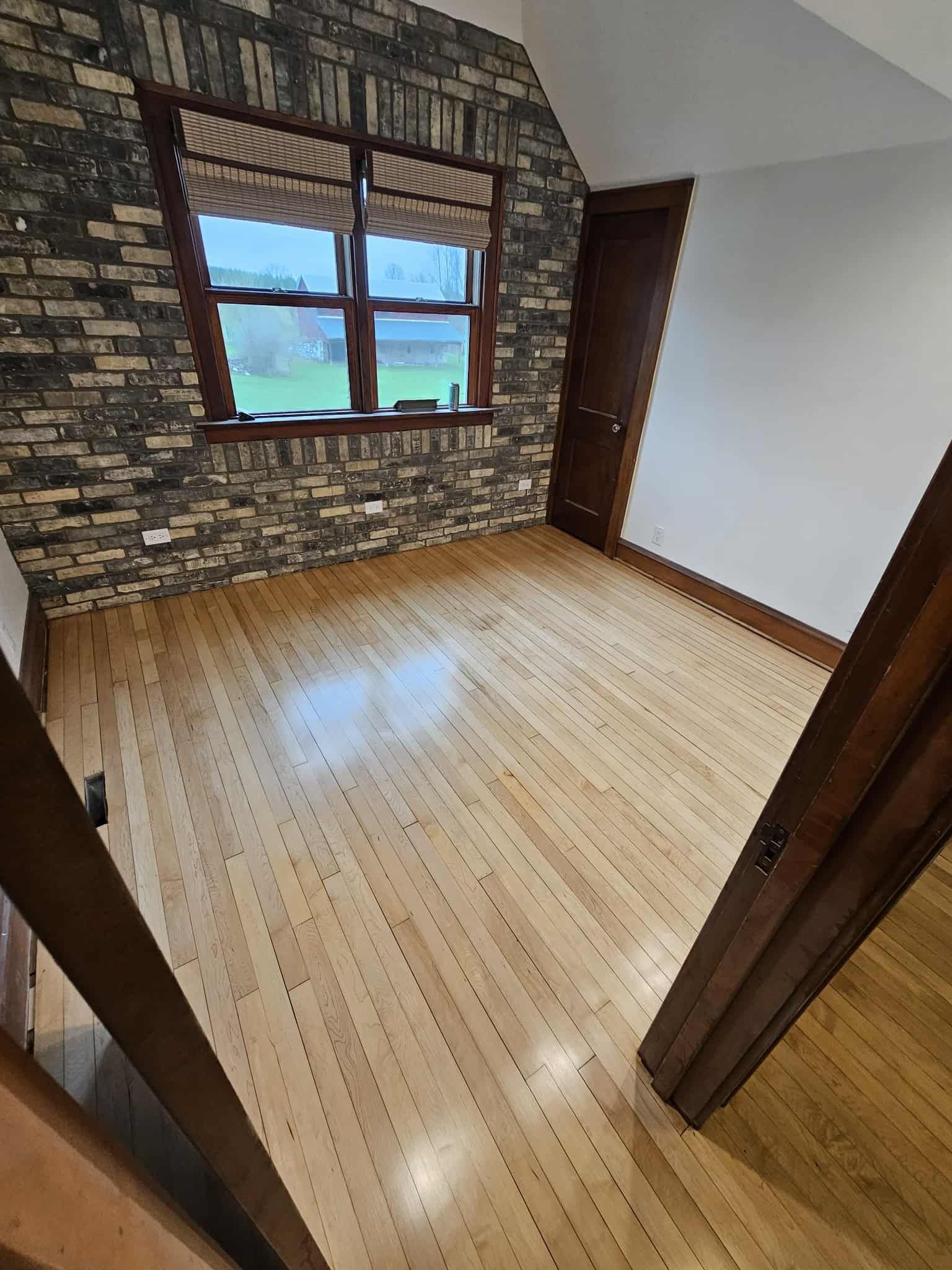 Empty room with wood floor, stone accent wall, window, and white walls.