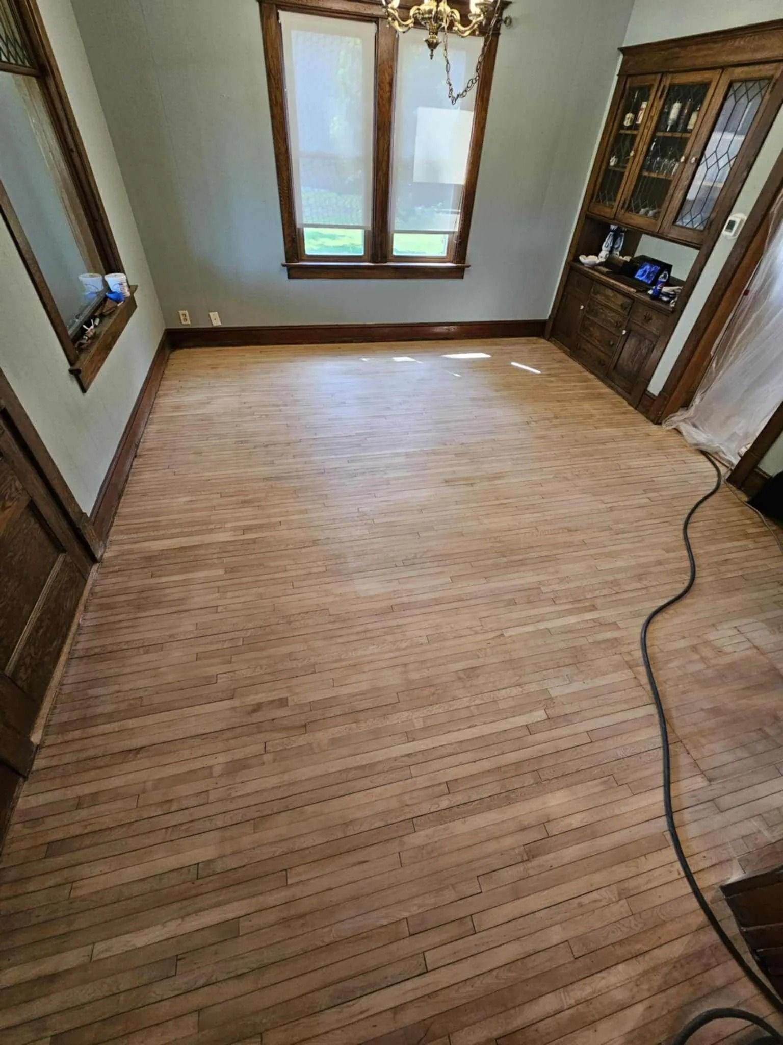 Empty room with light wood flooring, two windows, and a cabinet on the right.