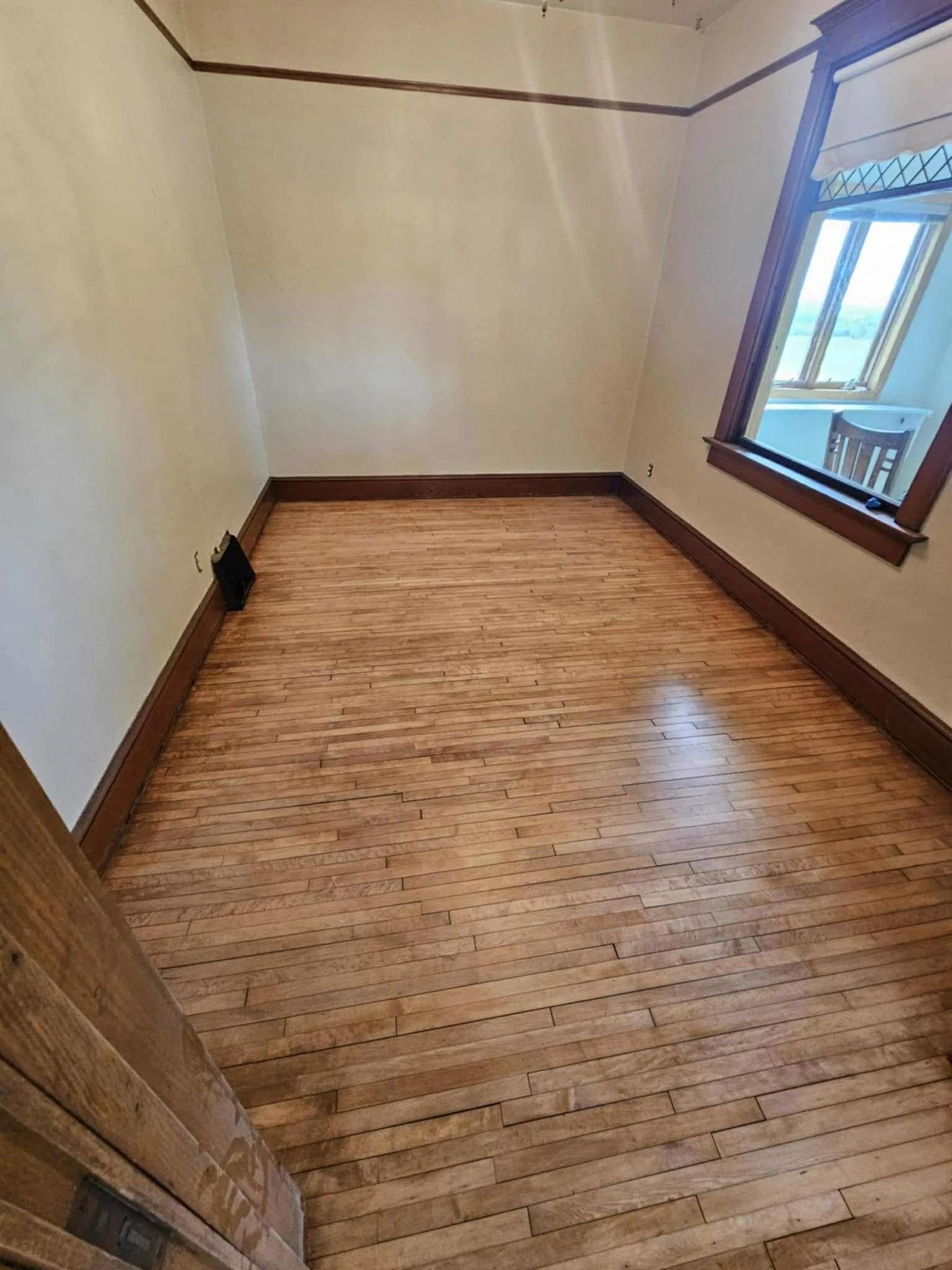 Empty room with wood floor, beige walls, and a window on the right.