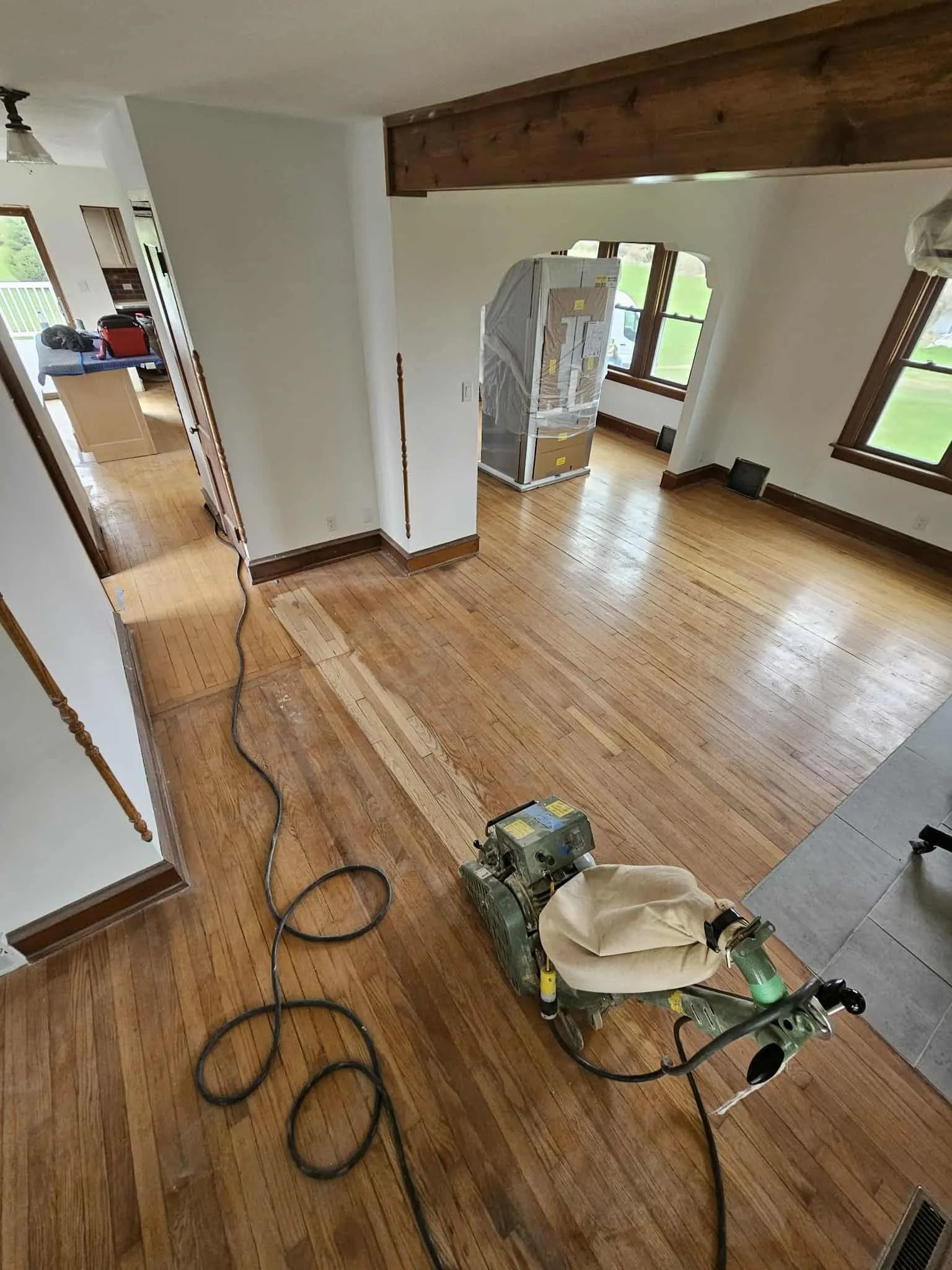 Room with freshly sanded wood floor, floor sander, and coiled cord in a partially renovated interior.