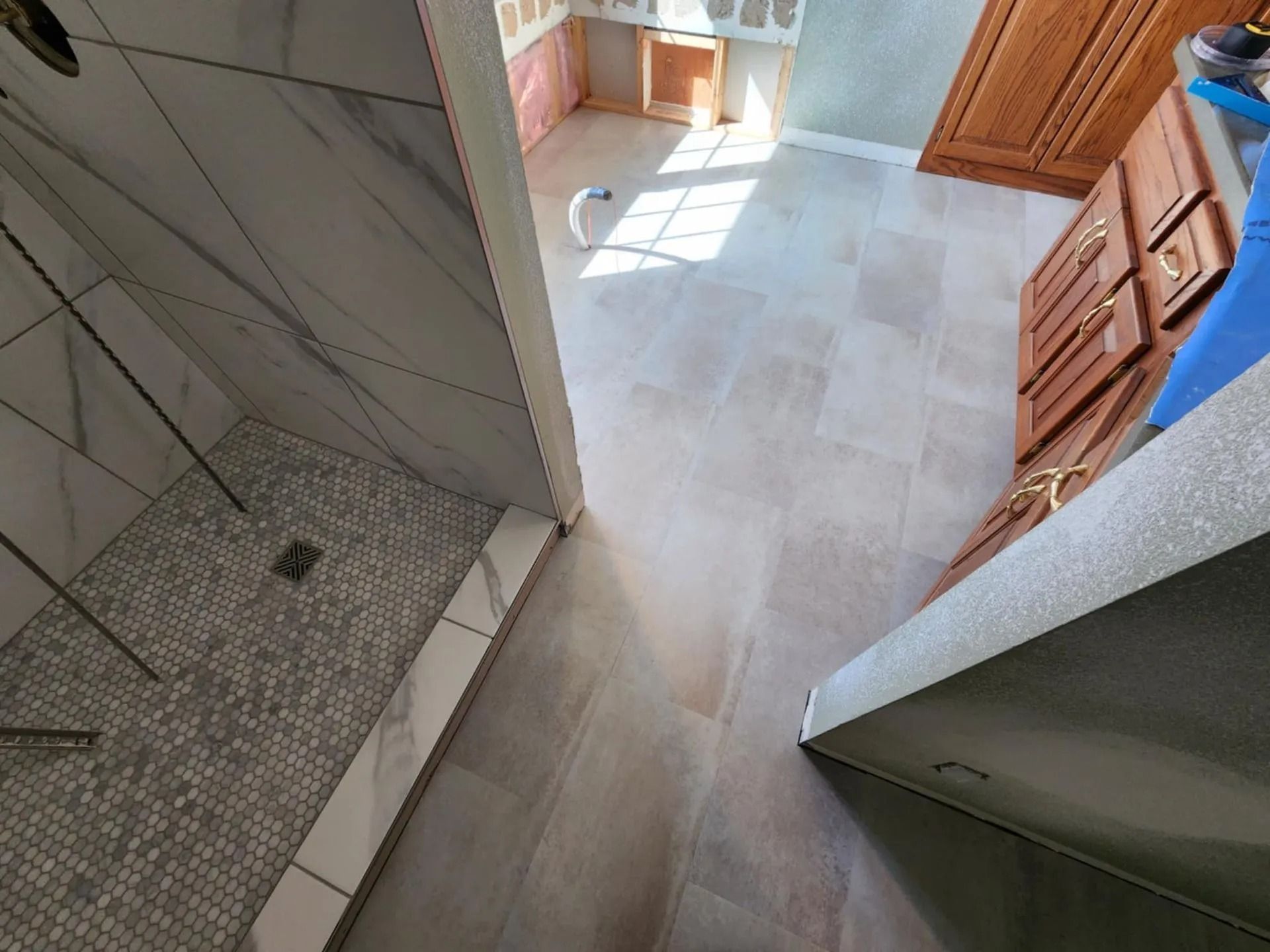 Interior hallway with tiled floor, staircase on the left, and sunlit doorway at the far end.