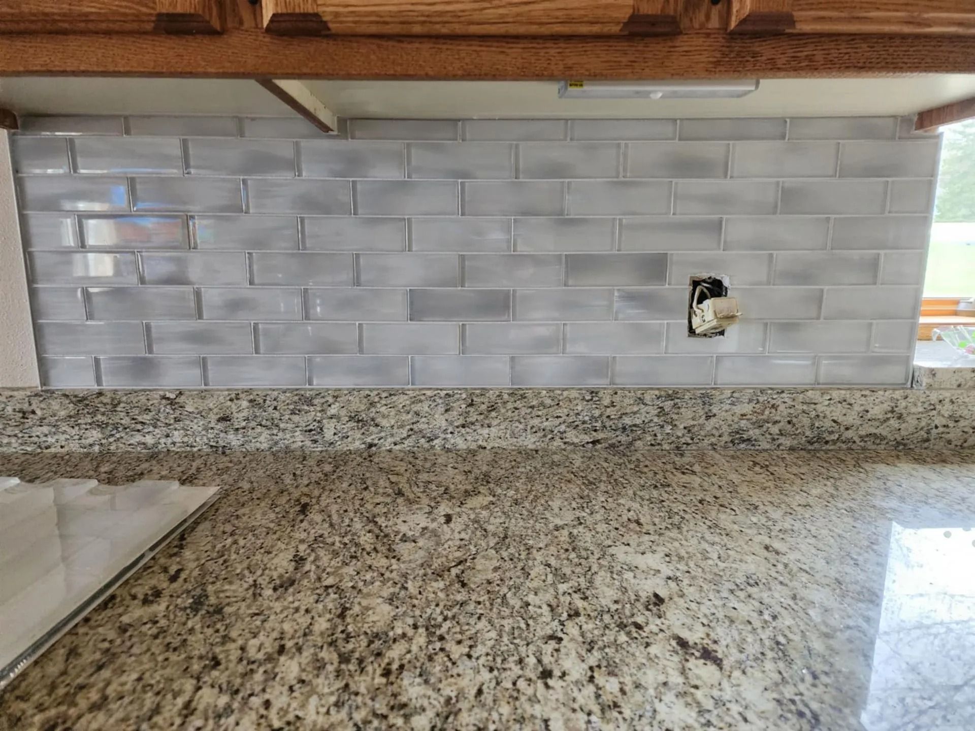 Kitchen counter with white subway tile backsplash and speckled granite countertop, showing an outlet hole.