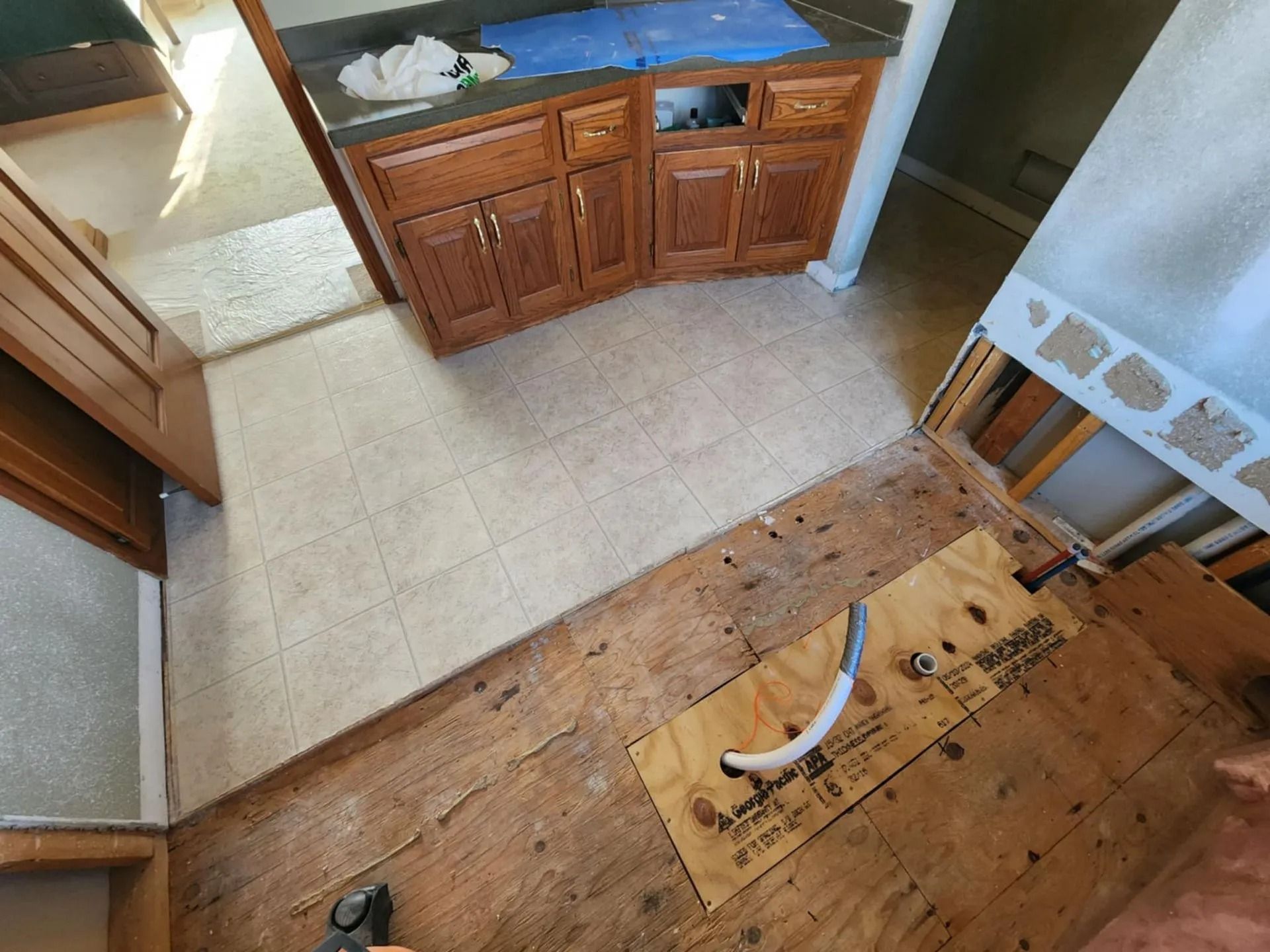 Damaged kitchen floor with exposed subfloor beside cabinets and a sink.