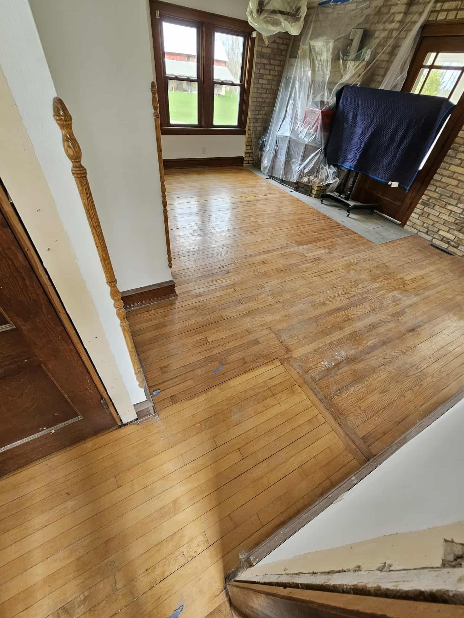 Empty room with worn wooden floors, a window, and covered furniture against the wall.