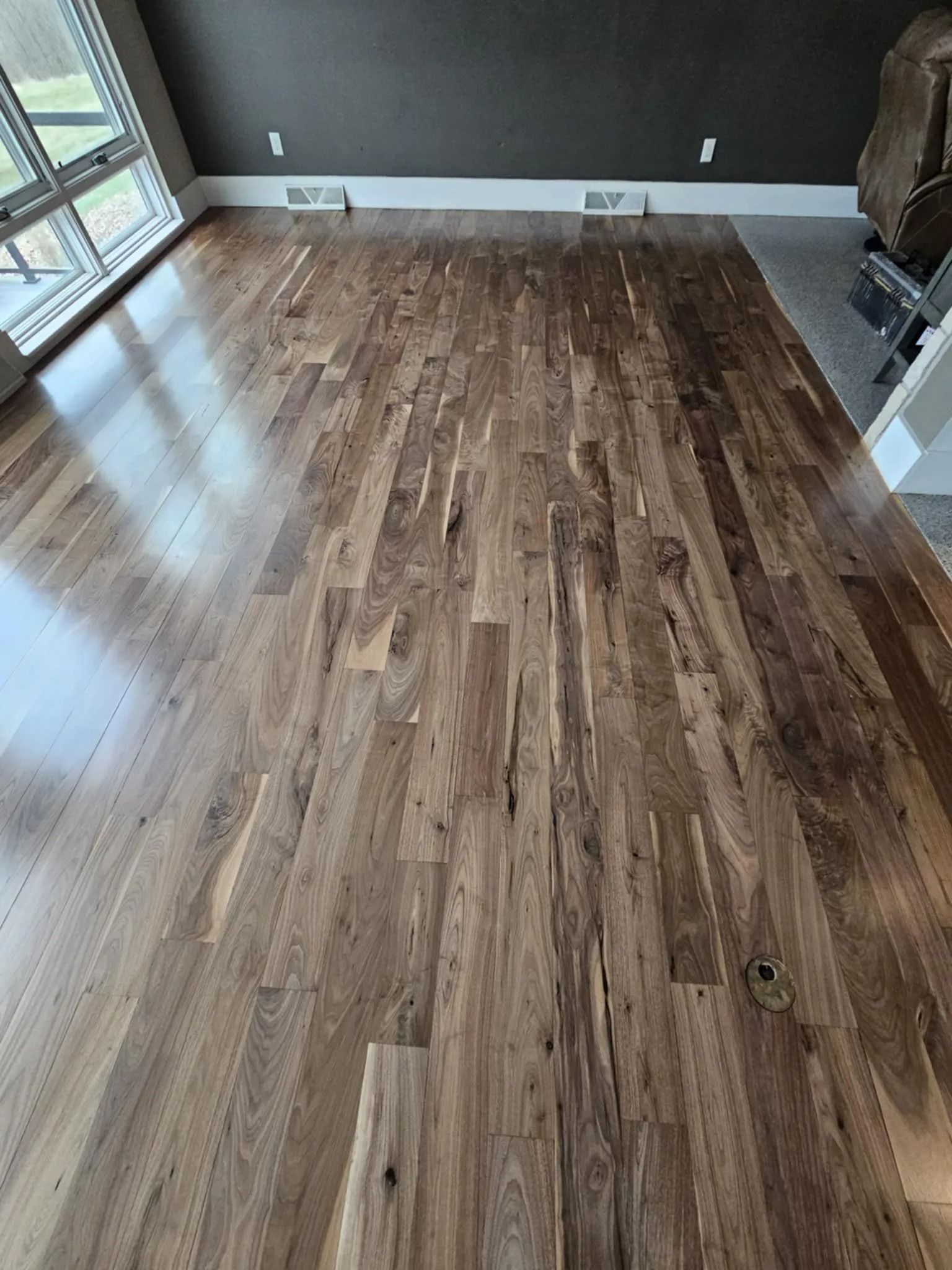 Empty room with wood-look flooring, dark walls, and windows letting in daylight.