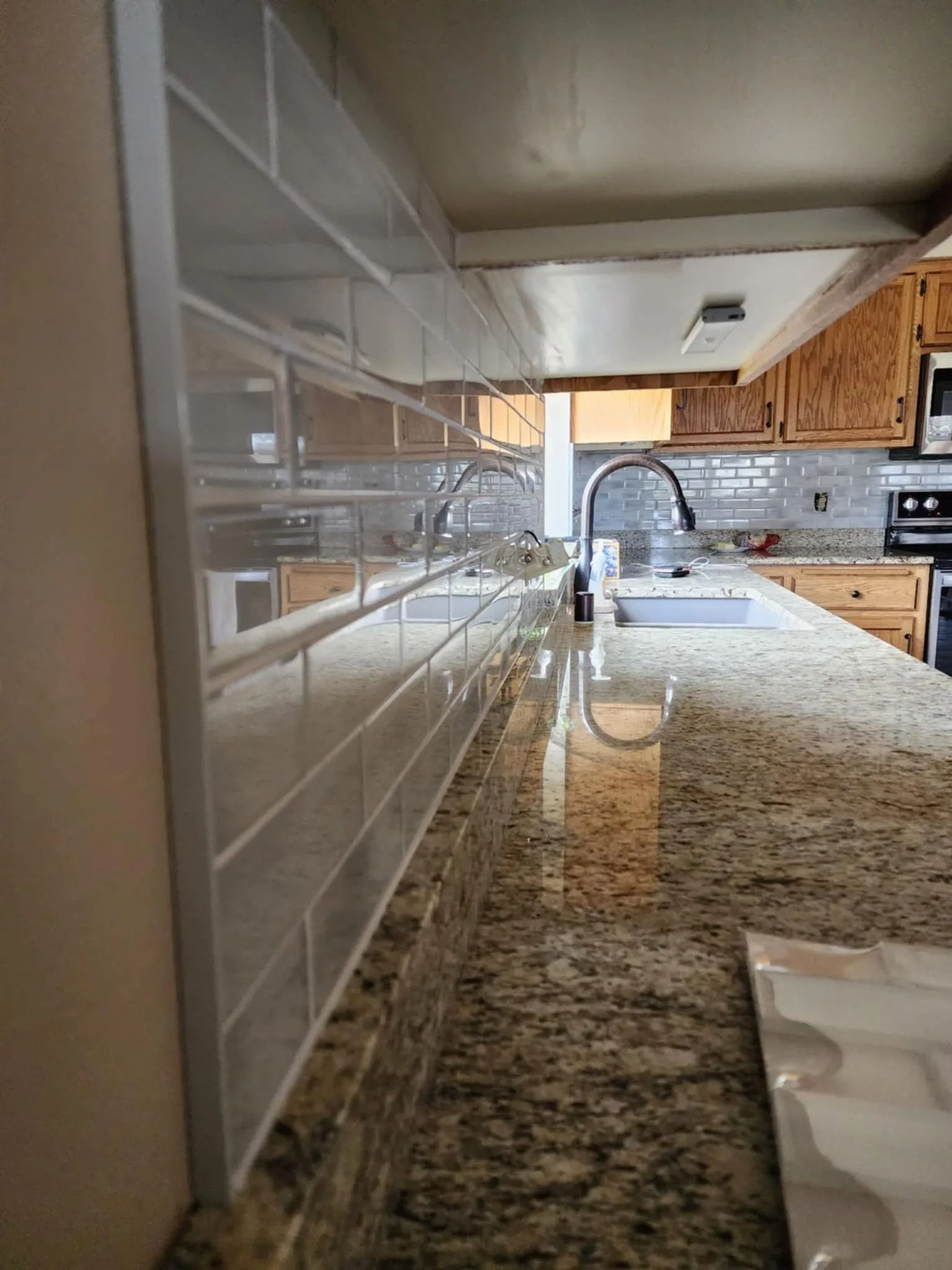 Kitchen countertop with granite surface, white tile backsplash, sink faucet, and wood cabinets in the background