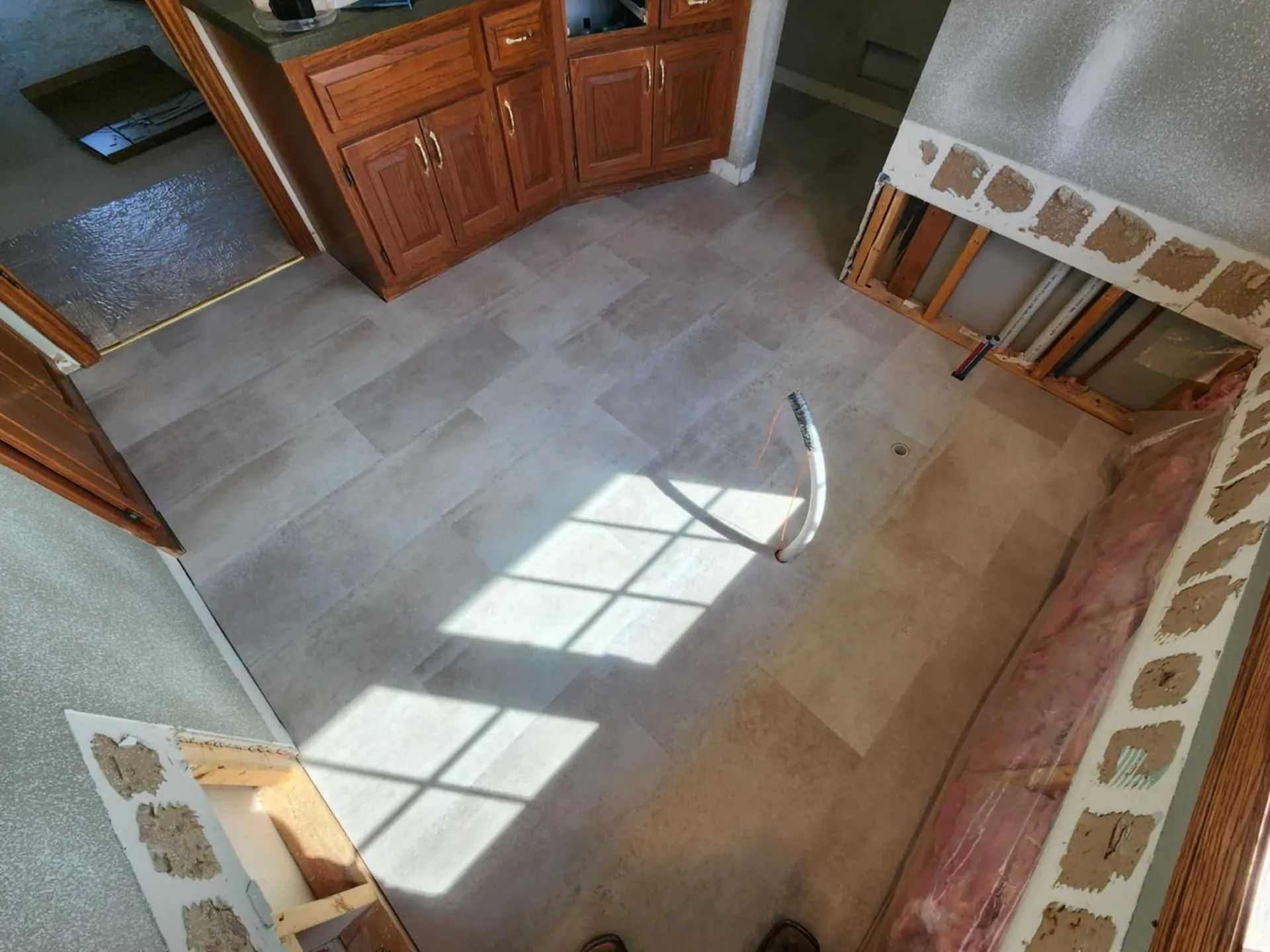 Empty tiled room with sunlight streaming through a window onto the floor and cabinets along one wall